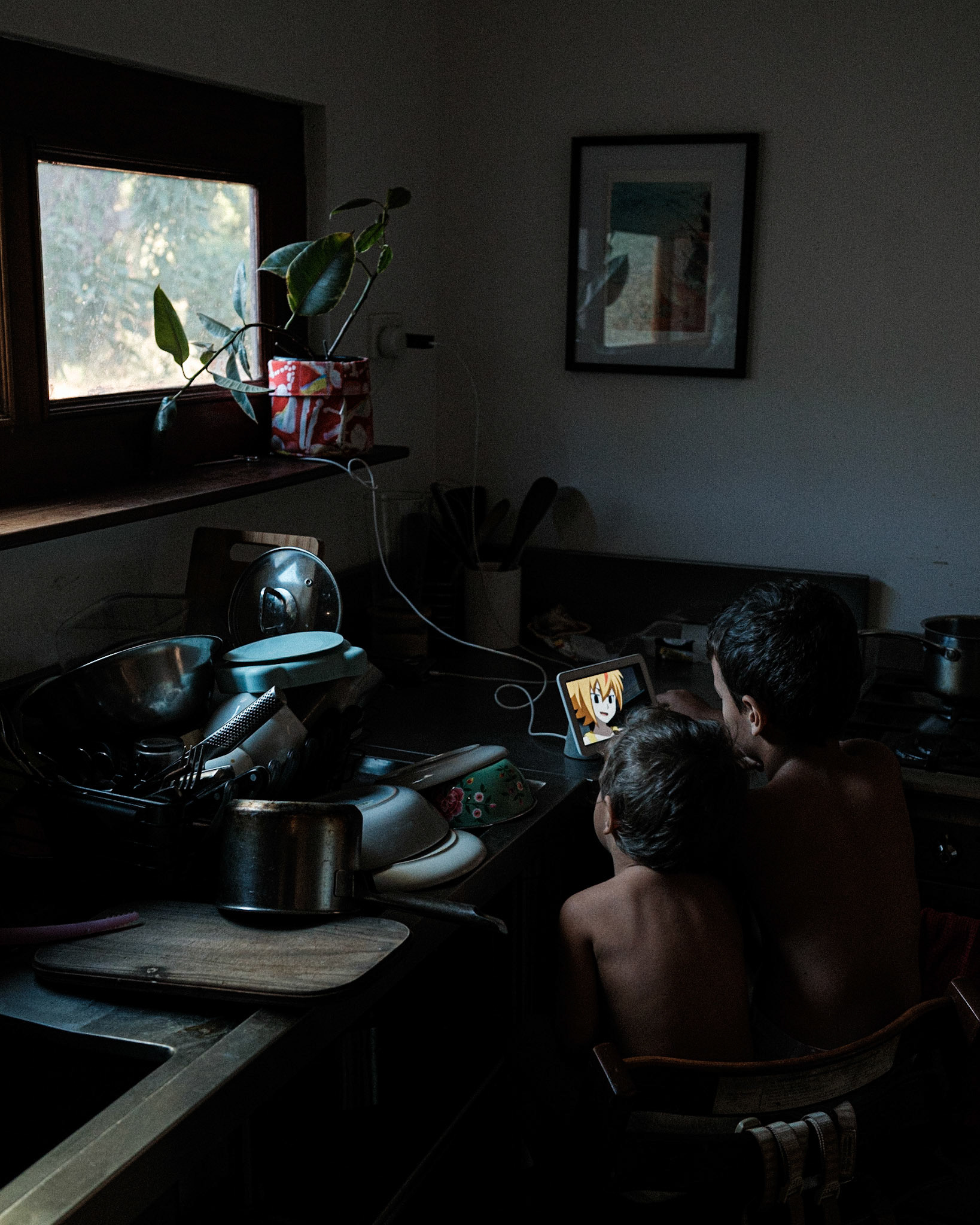 Bound by blood, rooted in solitude, the First Nation brothers find solace amidst the bleakness of their cluttered kitchen. In the feeble glow of a tiny screen, a Japanese anime character flickers, casting an eerie radiance that warms their desolate existence. The muted light dances upon their weary faces, revealing shadows of despair etched into their souls. With longing gazes, they seek refuge from their confinement, their eyes transfixed on the slender beam of nature's gift, a small plant reaching towards the stifled window. In this somber tableau, worlds collide, bridging cultures, as darkness and despair mingle with a fragile connection to life beyond their melancholic realm.