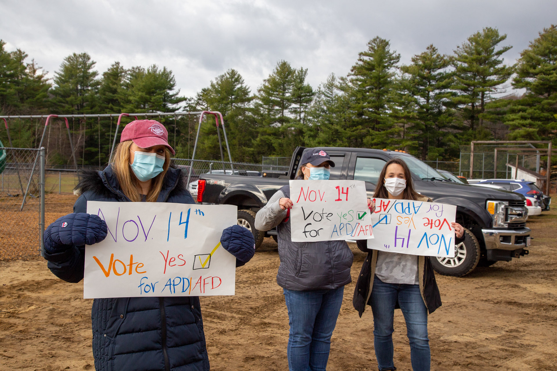 Three women stand with signs in support of a new building for the town. November 2020, Ashby, MA 