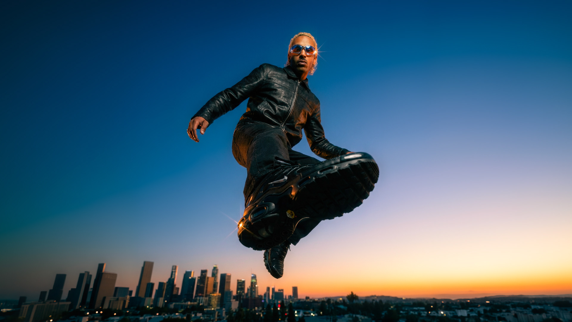 Homme en cuir noir et lunettes Oakley en lévitation au-dessus de la skyline de Los Angeles au crépuscule