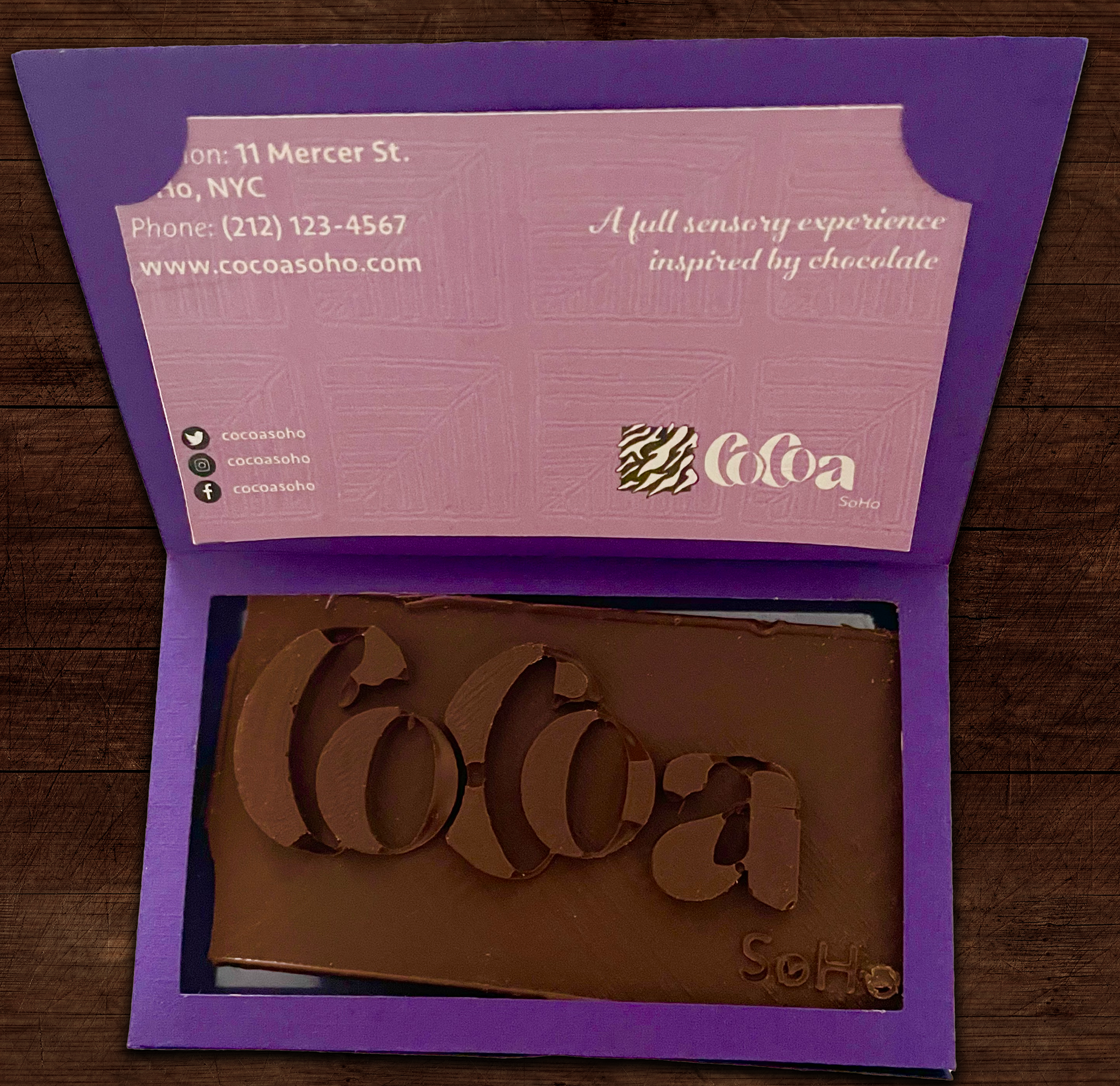 Business card holder (open). The chocolate was the hardest item to make during this entire project. I began the process by making a chocolate mold of our wordmark in Blender. After making a mold, I got the mold 3D printed with the help of a fellow classmate. With the mold complete, I bought food-safe silicon mold solution from a craft store. I poured the silicone and the 3D printed mold into a container. After it cured, I started making the chocolate by using melting wafers. Around 30 of these bars had to be made, which took around 15 hours in total (if you include melting, pouring, freezing, and cutting the excess). 