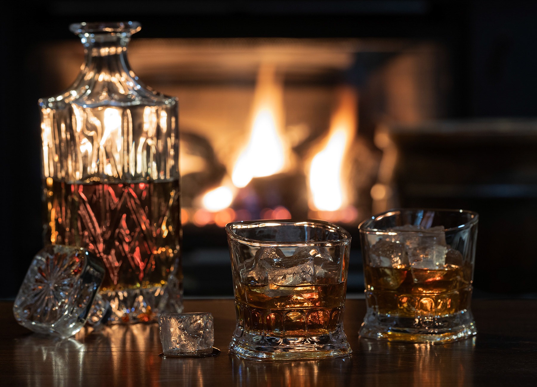 Glasses of wiskey with ice and decanter with fireplace in background