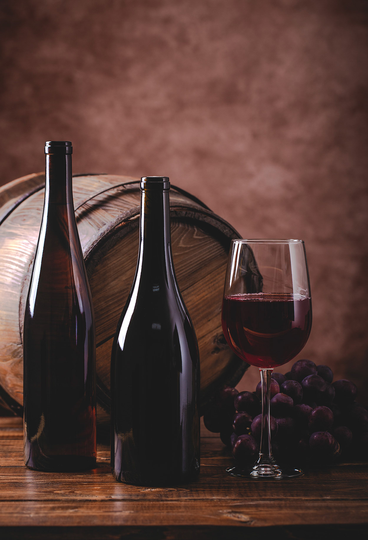 Glass of red wine and two bottles with grapes and wooden barrel