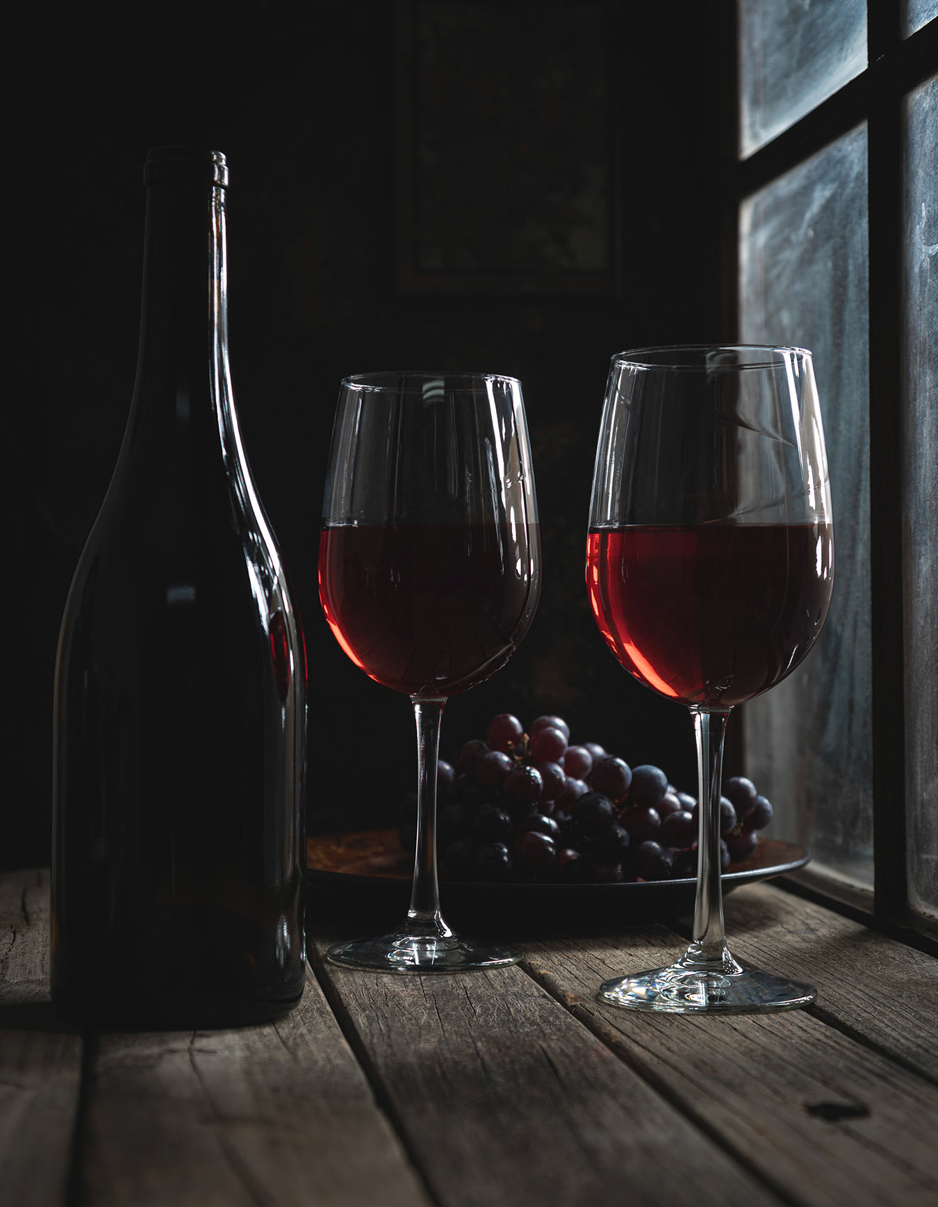 Glasses of red wine and bottle next to a window