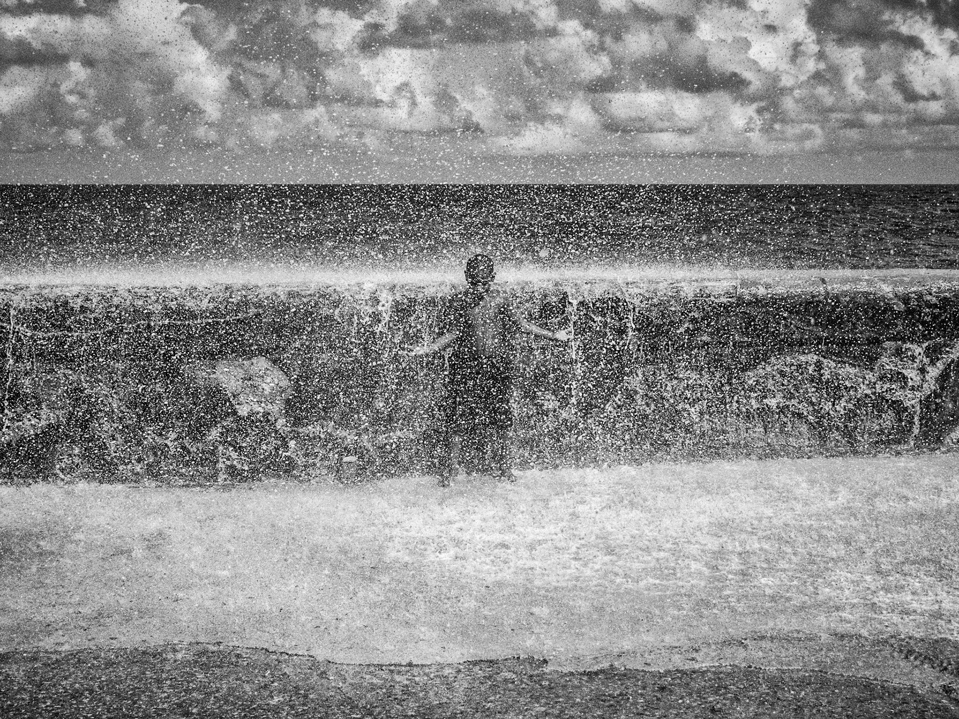Young Cuban boy playing and having fun in wave surf against the malecon seawall during high tide, Havana Cuba