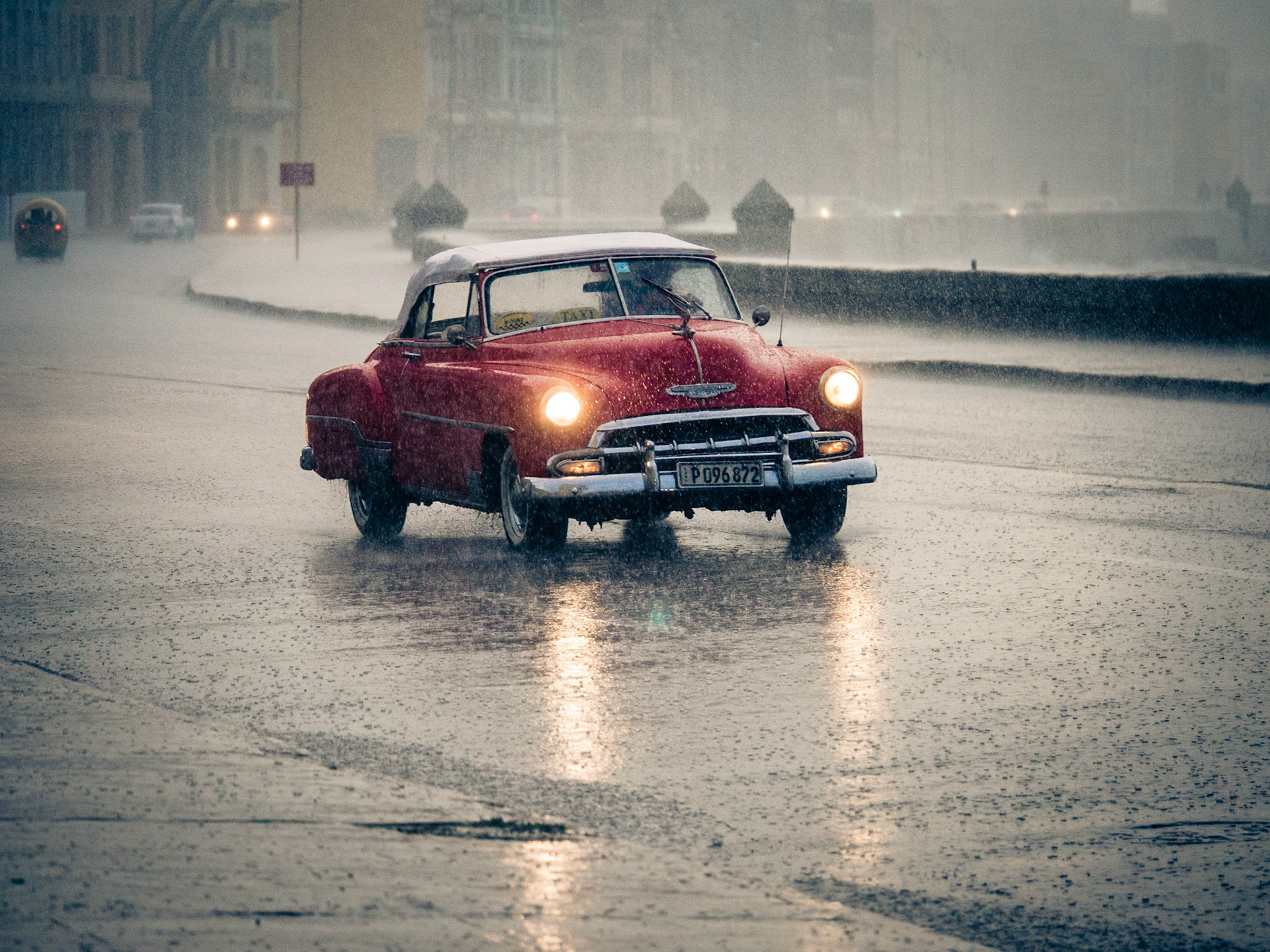 Red Cuban classic automobile taxi driving in heavy rain on The Malecon, Cuba, Caribbean