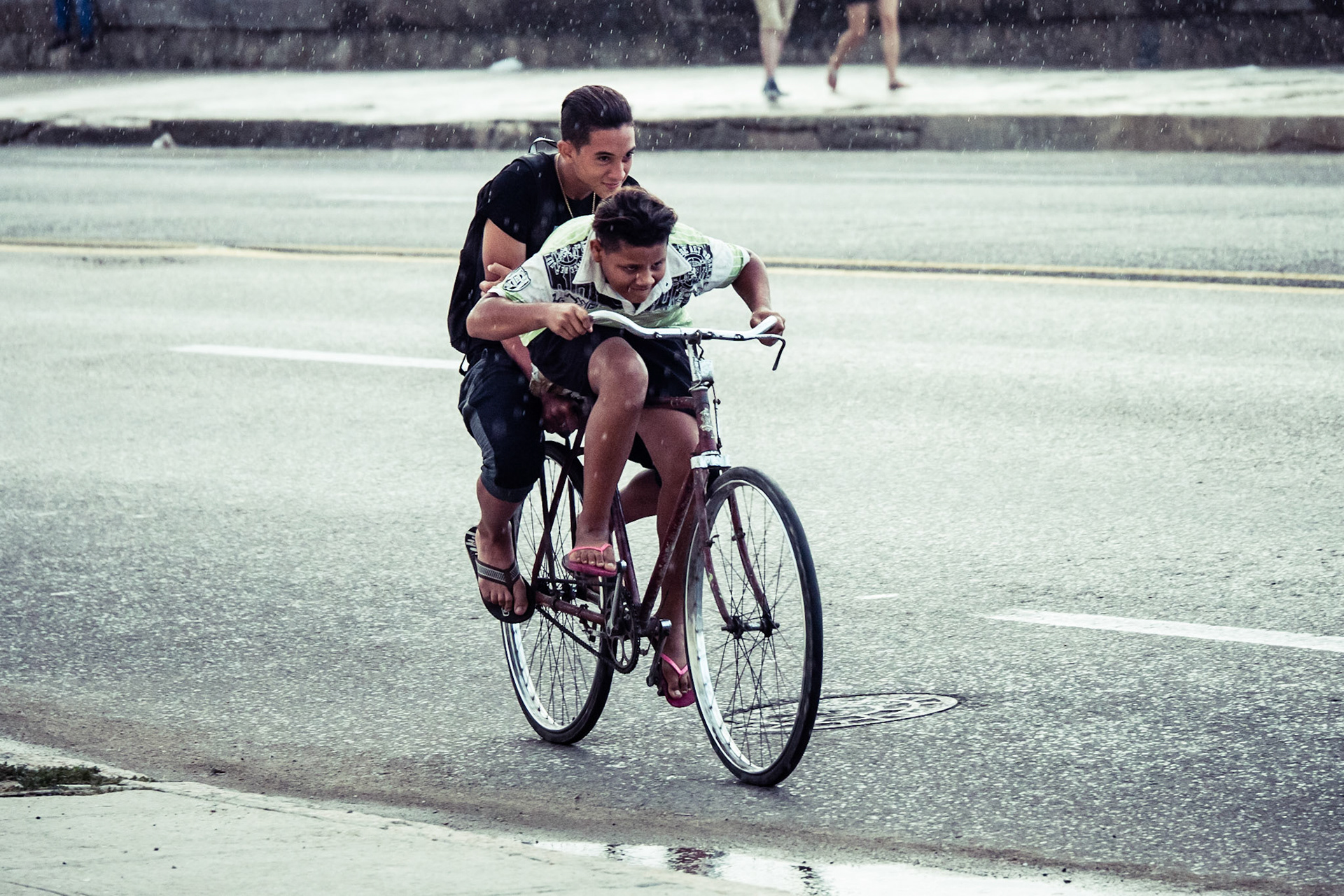 Two boys on a bicycle in heavy rain on The Malecon, Havana, Cuba