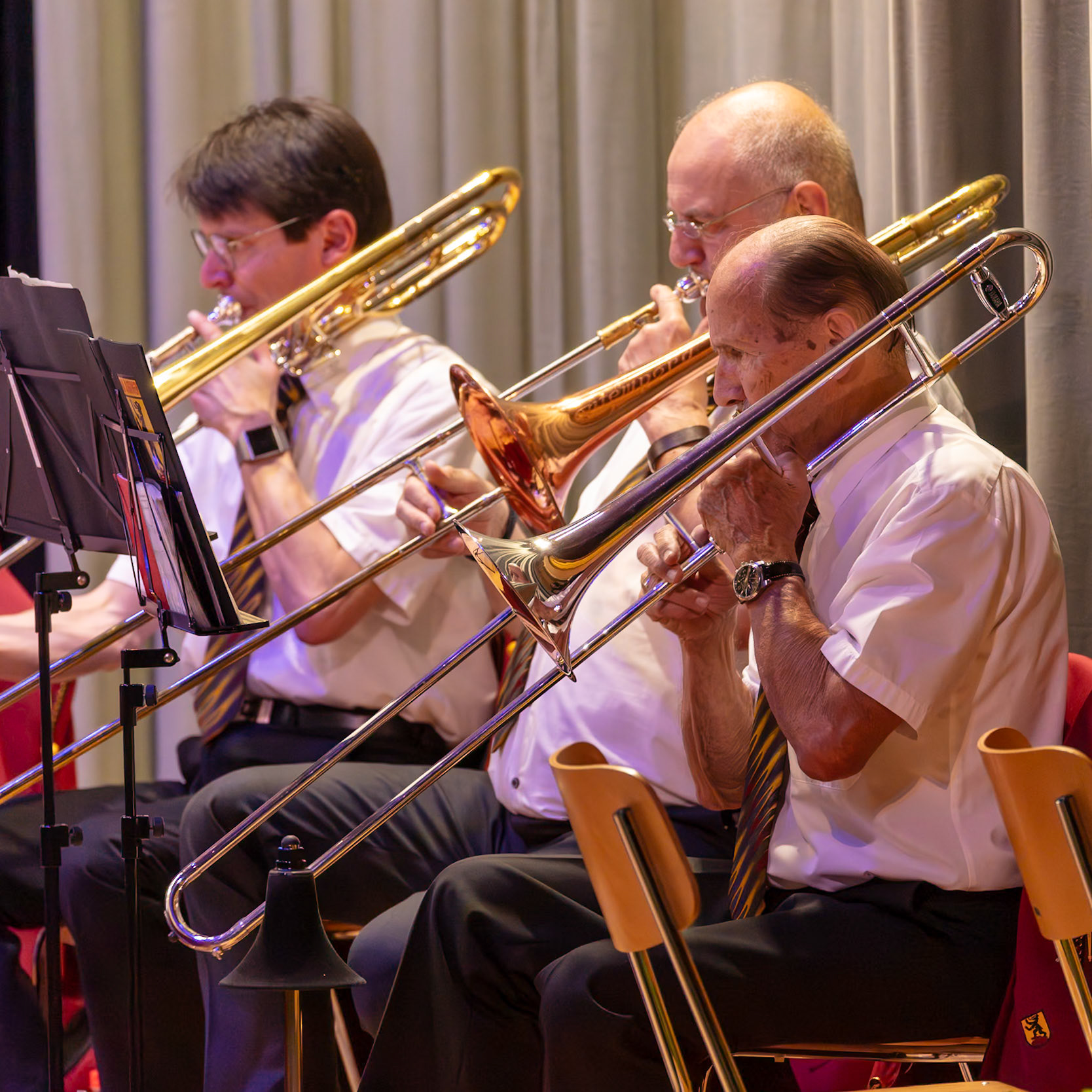 Eine Brassband spielt im Konzert.  Mehrere Musiker, darunter [Name des Musikers 1] (Trompete), [Name des Musikers 2] (Trompete) und [Name des Musikers 3] (Posaune), spielen leidenschaftlich auf ihren Instrumenten.  Sie konzentrieren sich auf die Musik und die präzise Ausführung der Noten.  Die Atmosphäre ist konzentriert und voller musikalischer Energie.  Das Bild zeigt die Leidenschaft und die Präzision, die in einem Orchester- oder Brassband-Konzert erforderlich sind.