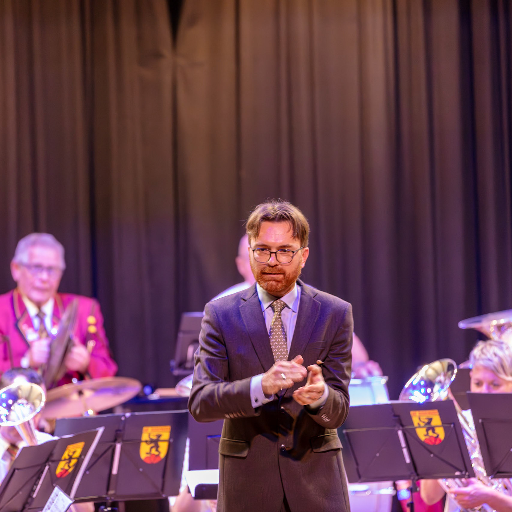 Ein Dirigent, vermutlich Herr [Name des Dirigenten, falls bekannt], dirigiert eine Blaskapelle.  Die Musikerinnen und Musiker der Kapelle spielen auf ihren Instrumenten, vermutlich Brass-Instrumente.  Der Dirigent gibt Anweisungen, um die Musik synchron und rhythmisch zu gestalten.  Die Atmosphäre ist konzentriert und professionell, wie man sie bei einem Konzert oder einer öffentlichen Aufführung erwartet.