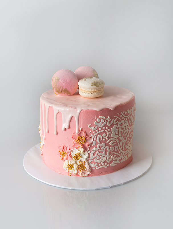 Ribbon cake with white chocolate drips decorated with butter cream using a stencil and knife art. Topped off with 03 Macaroons
