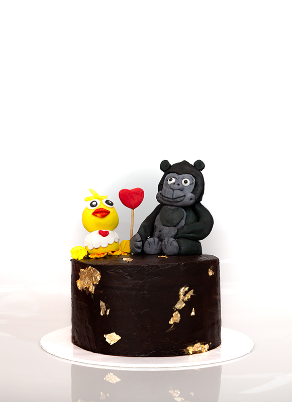 Chocolate cake with butter cream frosting with golden foil decorations and animals made out of fondant
