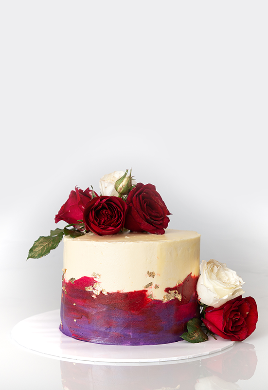 Vanilla cake coated with butter cream frosting garnished with fresh red roses