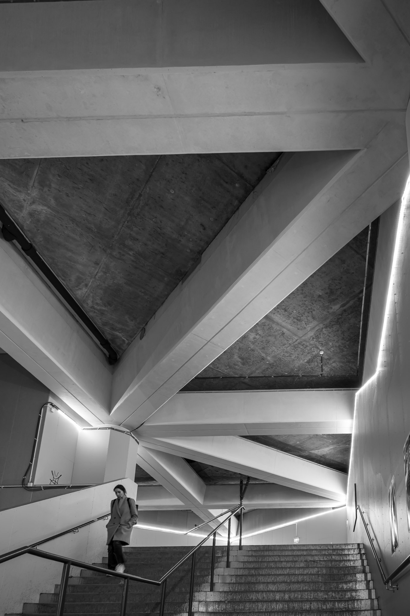 A person ascends a modern concrete staircase under geometric ceiling structures with ample lighting.