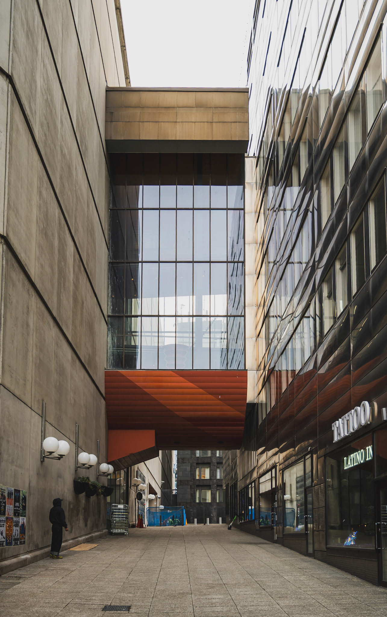 A narrow urban alleyway features a striking modern building with a large glass window and red accents.