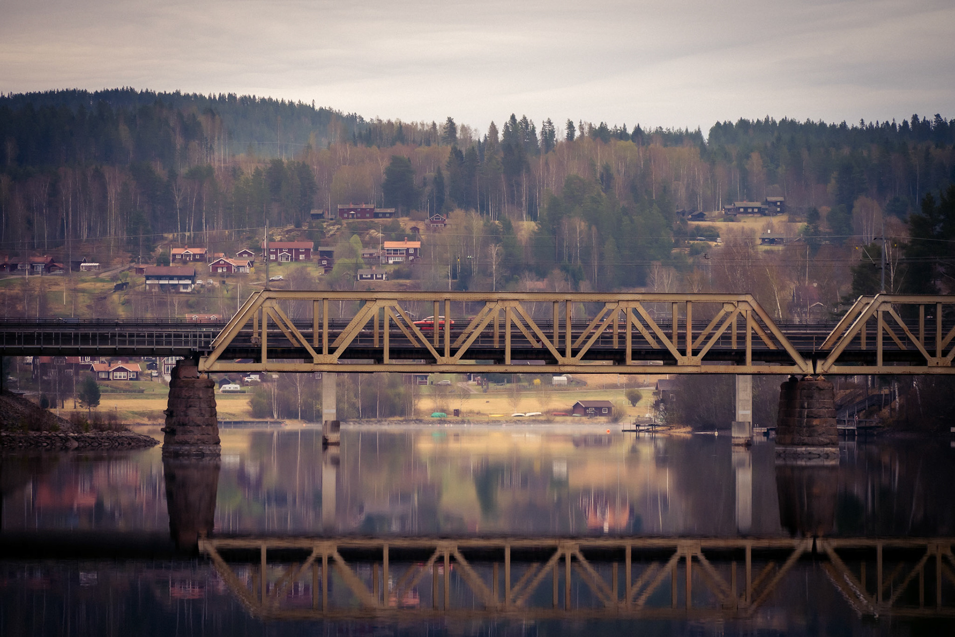 A serene landscape featuring a bridge spanning a calm river, with a forested town in the background.
