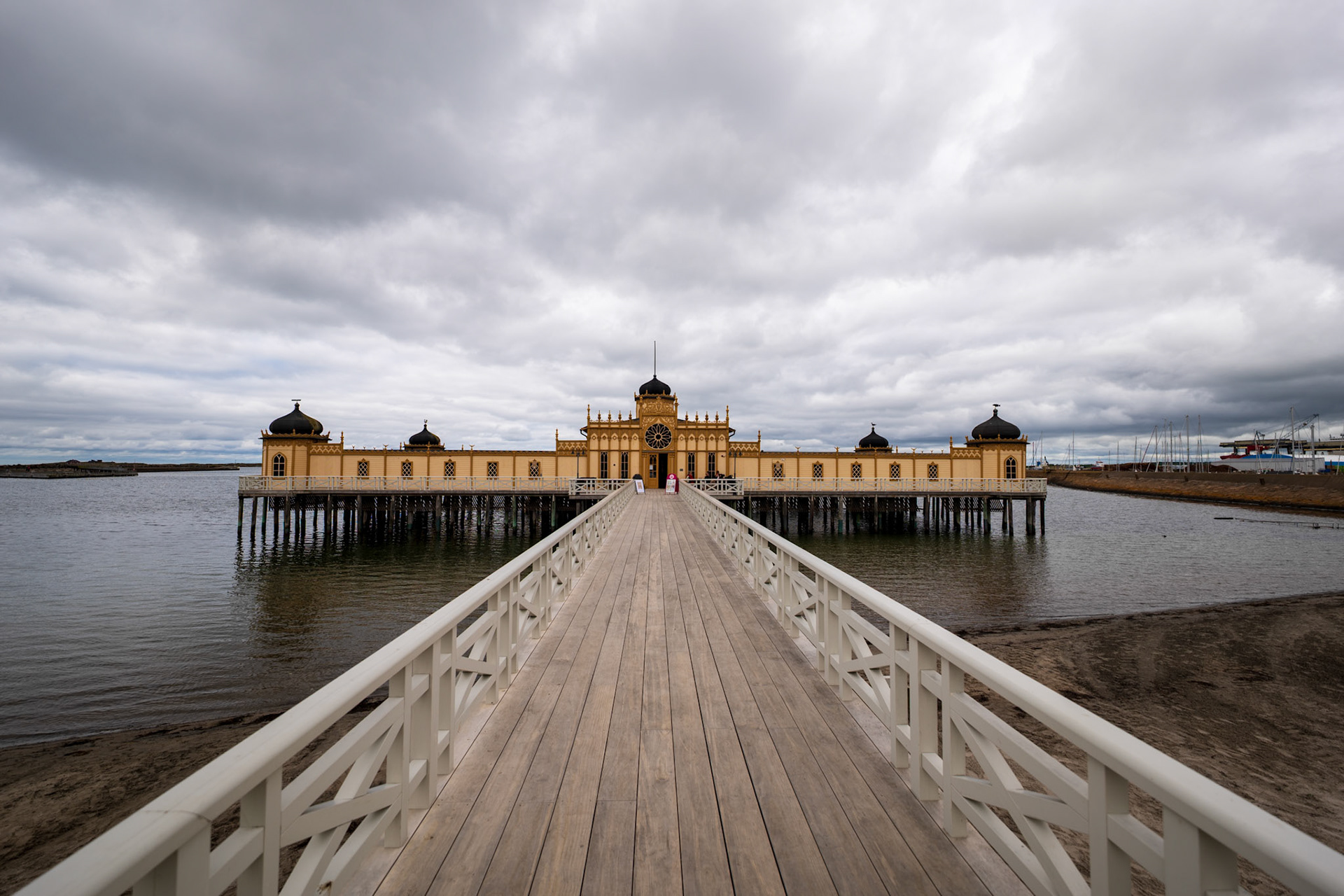 A weathered wooden pier with railings extends into a body of water under a cloudy sky.