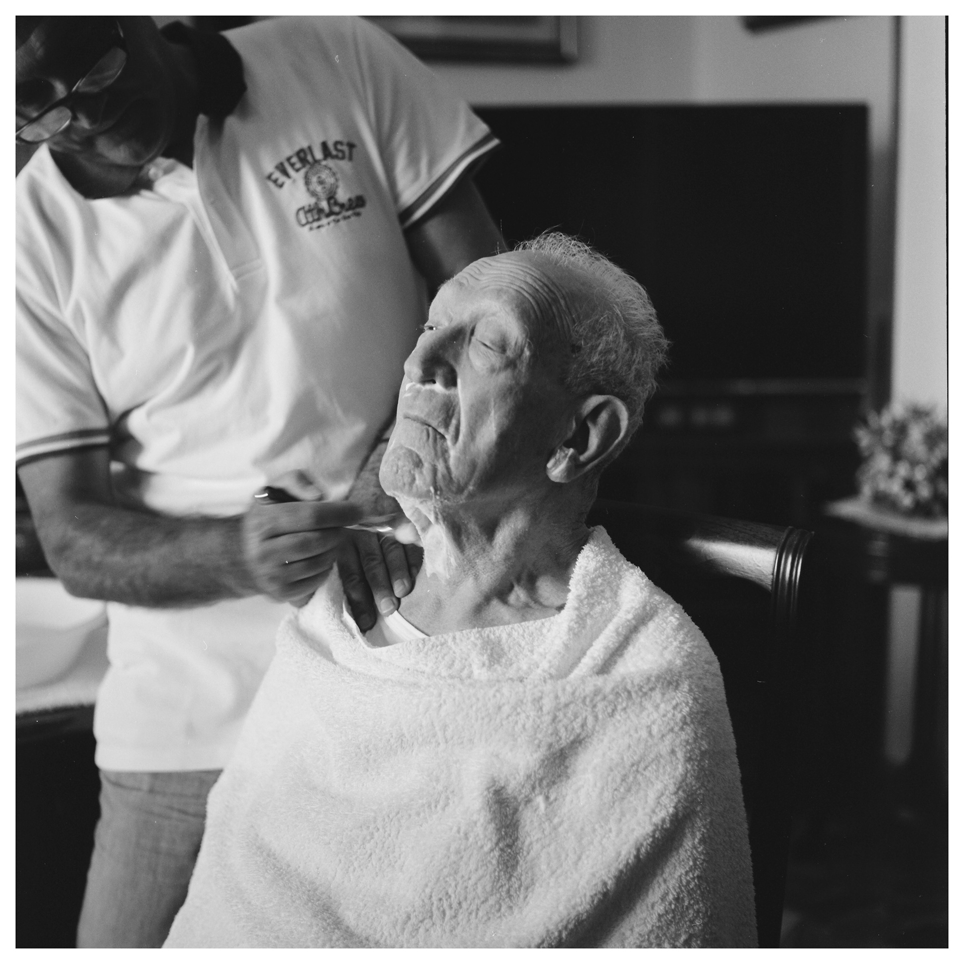 Foto in bianco e nero di un uomo che taglia la barba al padre in casa - progetto autoriale Andrea Palumbo fotografosuo padre