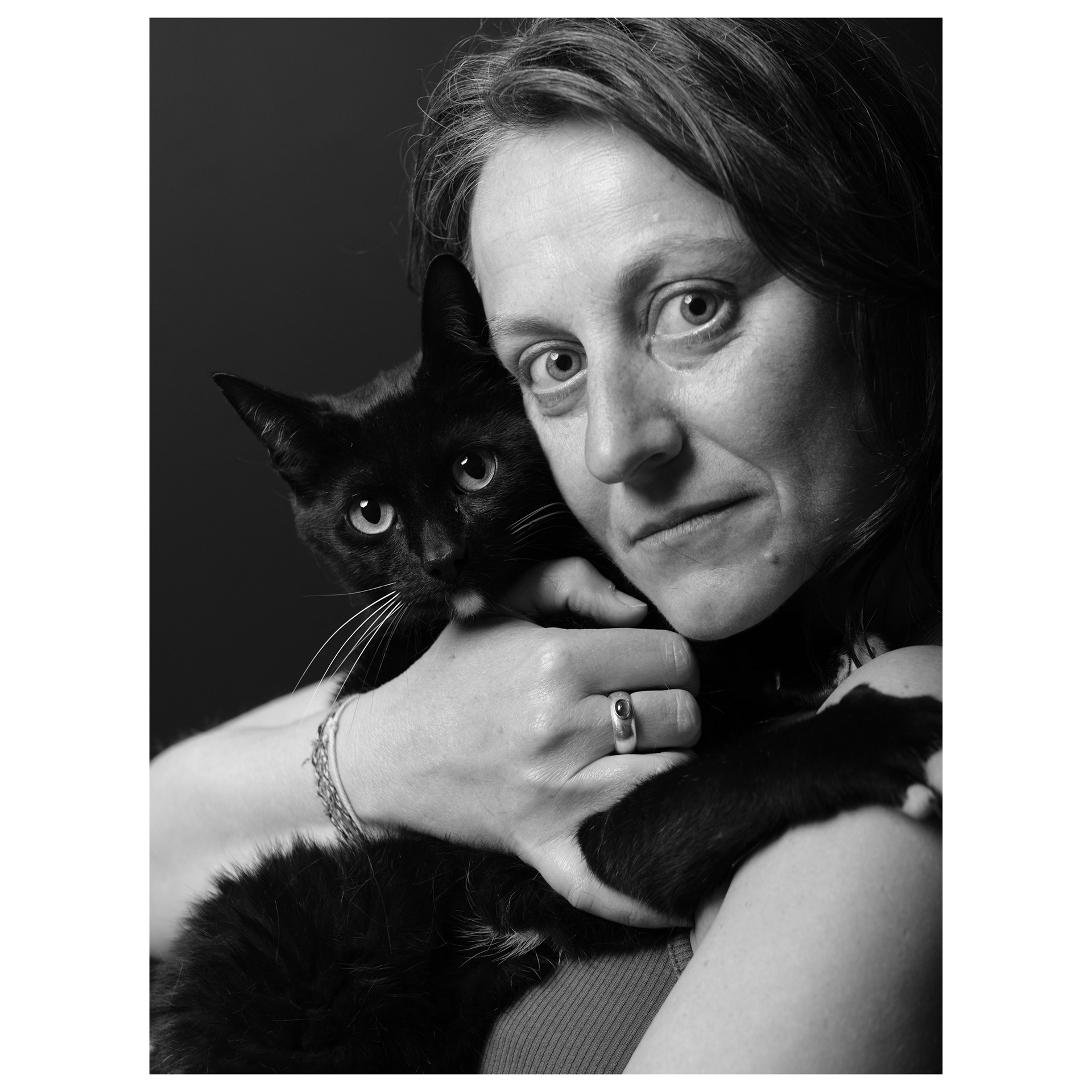 Ritratto fotografico in studio con sfondo nero di una donna dagli occhi verdi con gatto nero in braccio 