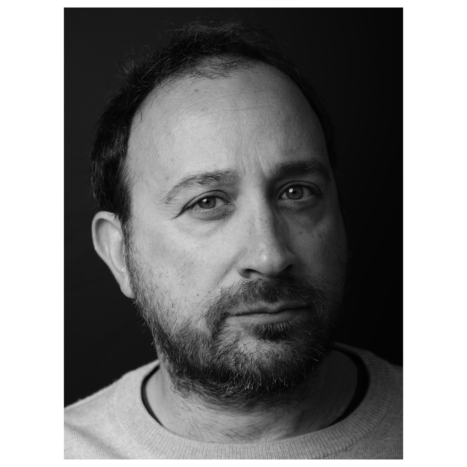 Ritratto fotografico in bianco e nero con flash e sfondo nero di un uomo che guarda in macchina
