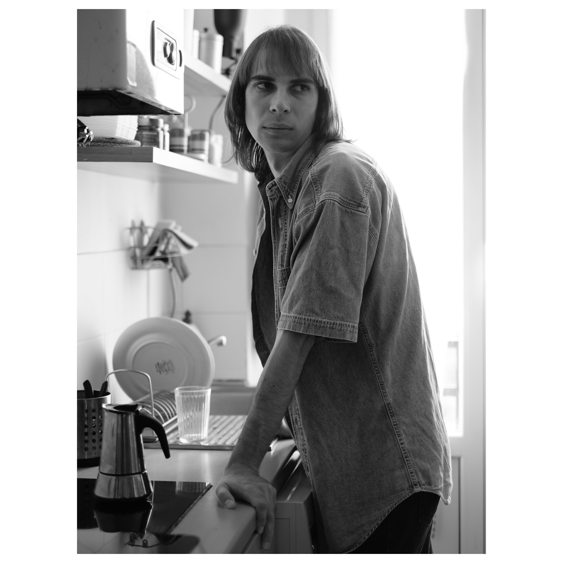 Ritratto in bianco e nero di Alessio appoggiato al bancone della sua cucina mentre guarda di lato - progetto fotografico di Andrea Palumbo