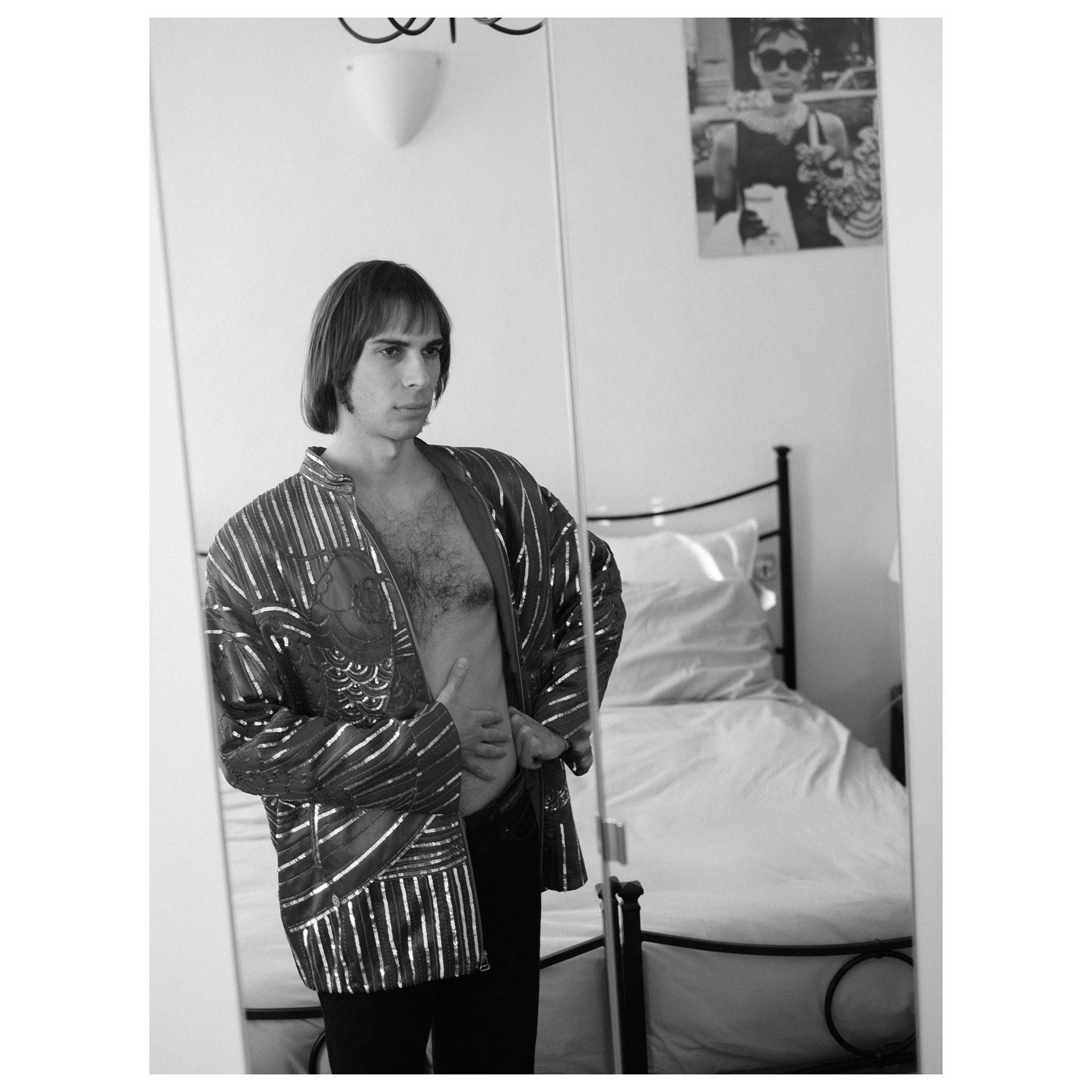 Foto in bianco e nero di uno specchio che riflette l'immagine di Alessio che prova una giacca sgargiante un po' vintage - progetto fotografico di Andrea Palumbo