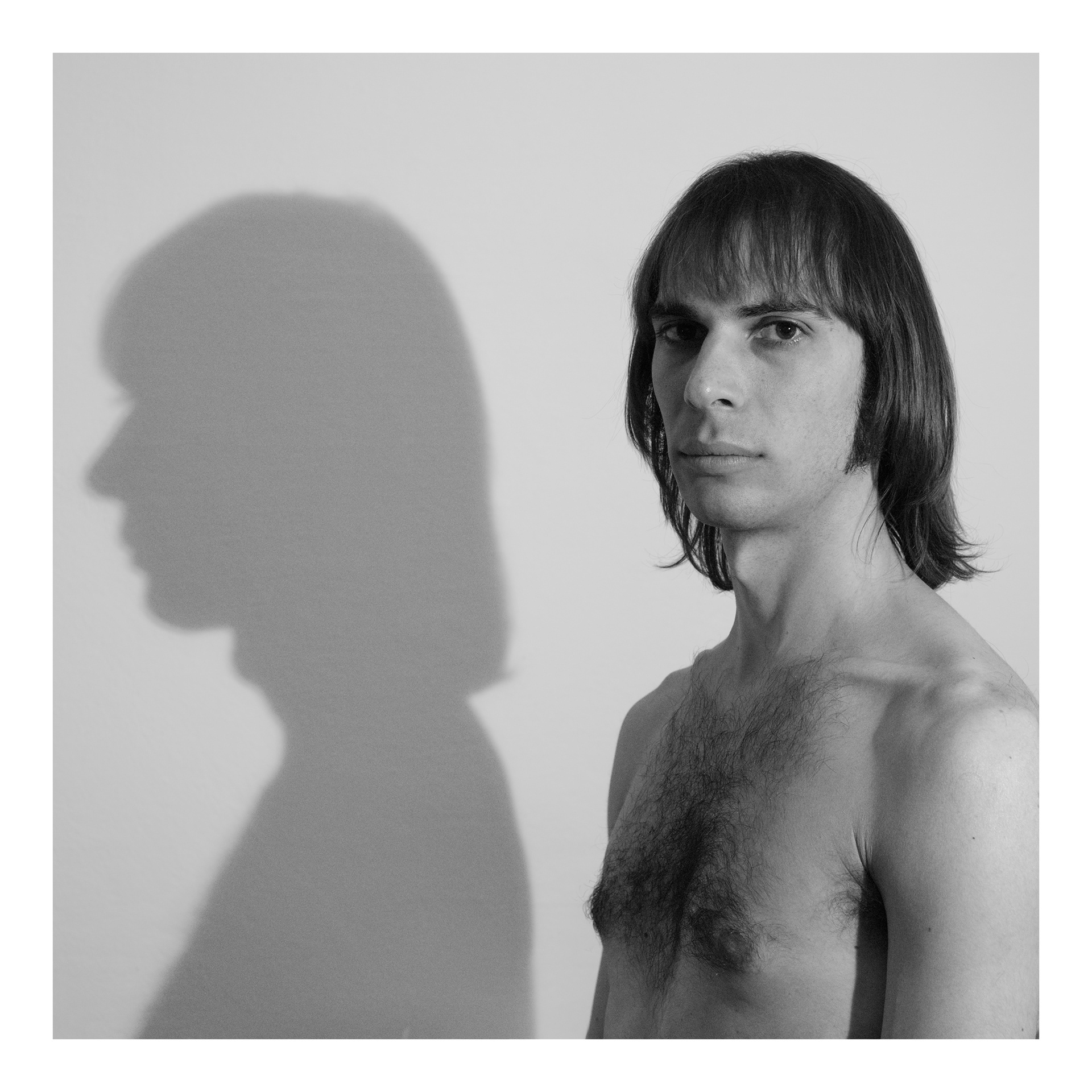 Foto in bianco e nero di Alessio vicino a una parete con l' ombra del suo profilo molto netta proiettata sul muro - progetto fotografico di Andrea Palumbo