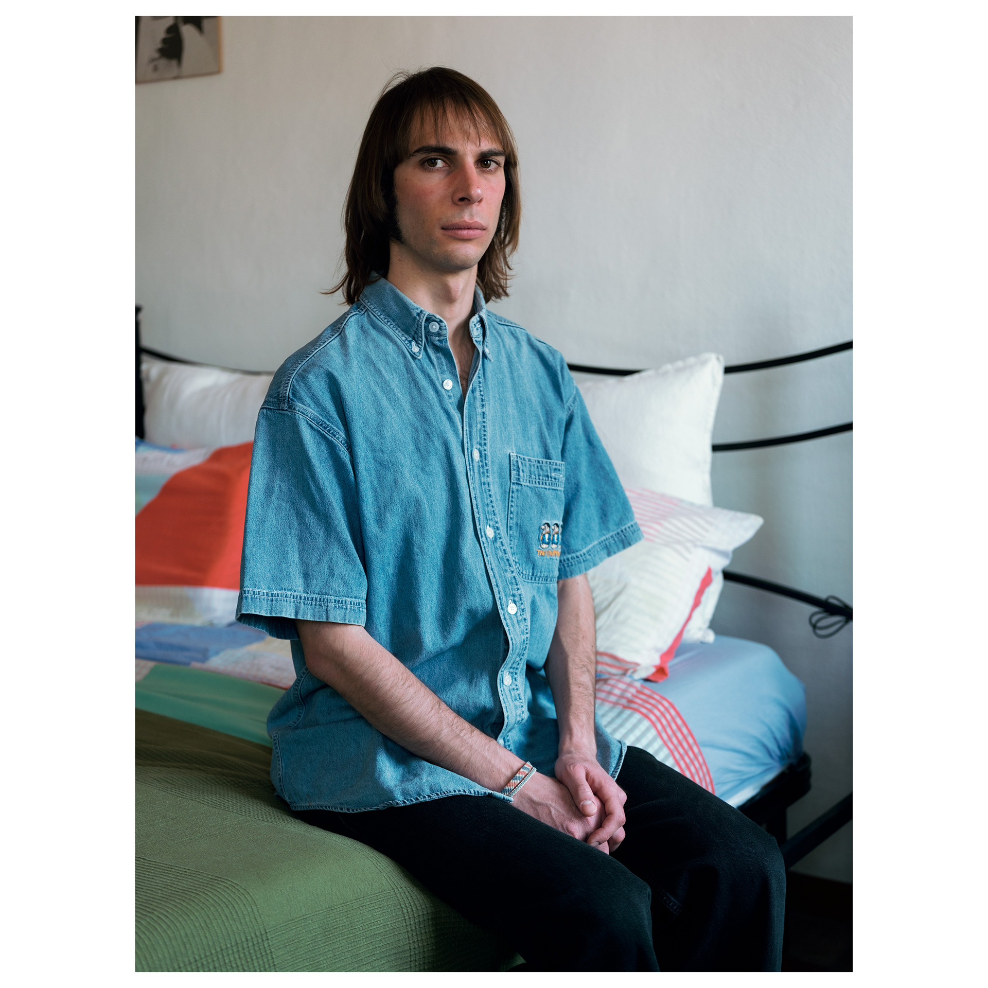 Ritratto a colori di Alessio seduto sul letto e con sguardo serio in macchina - progetto fotografico di Andrea Palumbo