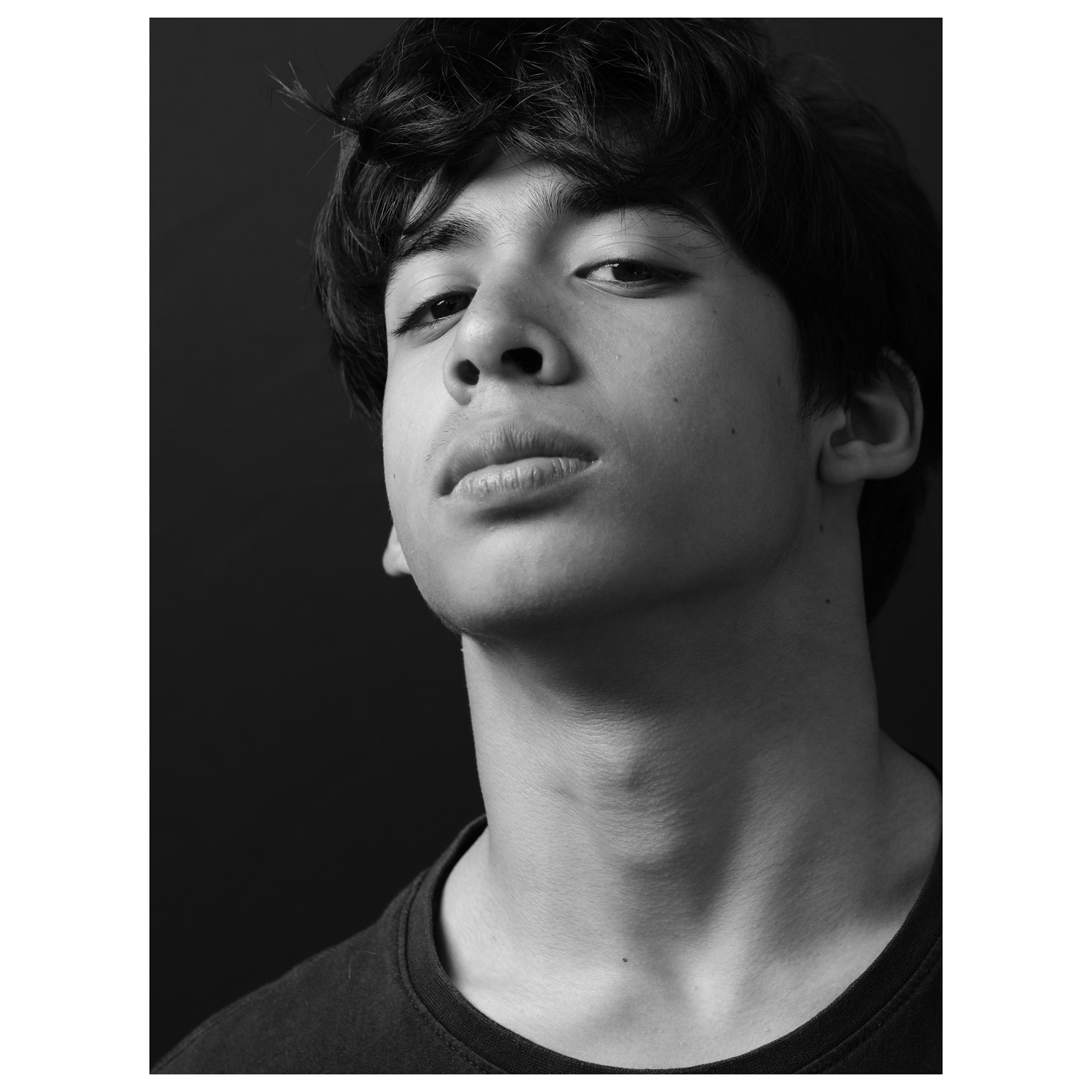 Ritratto fotografico in bianco e nero con flash e sfondo nero di un ragazzo con l'espressione da duro 