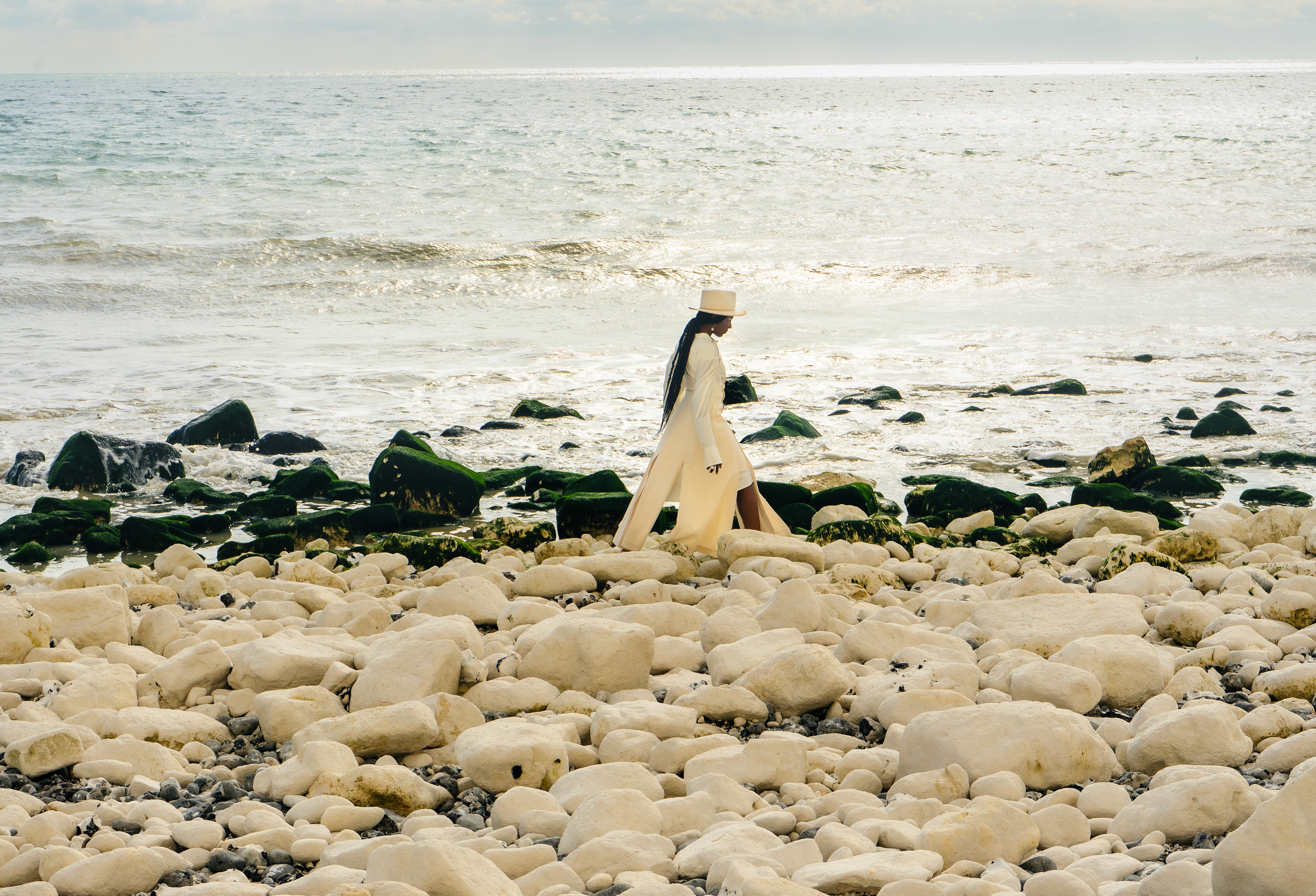 Fashion Editorial shot with a black model. Wearing an all white outfit as she walks along the shore side. Creative Director – Rohmarra Kerr Photographer – Amin McDonald BTS Photographer – Gemma Alexander Stylist – Kirsty Peters Makeup Artist – Sofia Mazurendo Model – Aaliyah AileruShot by Amin McDonald, featured in Noctis Magazine.