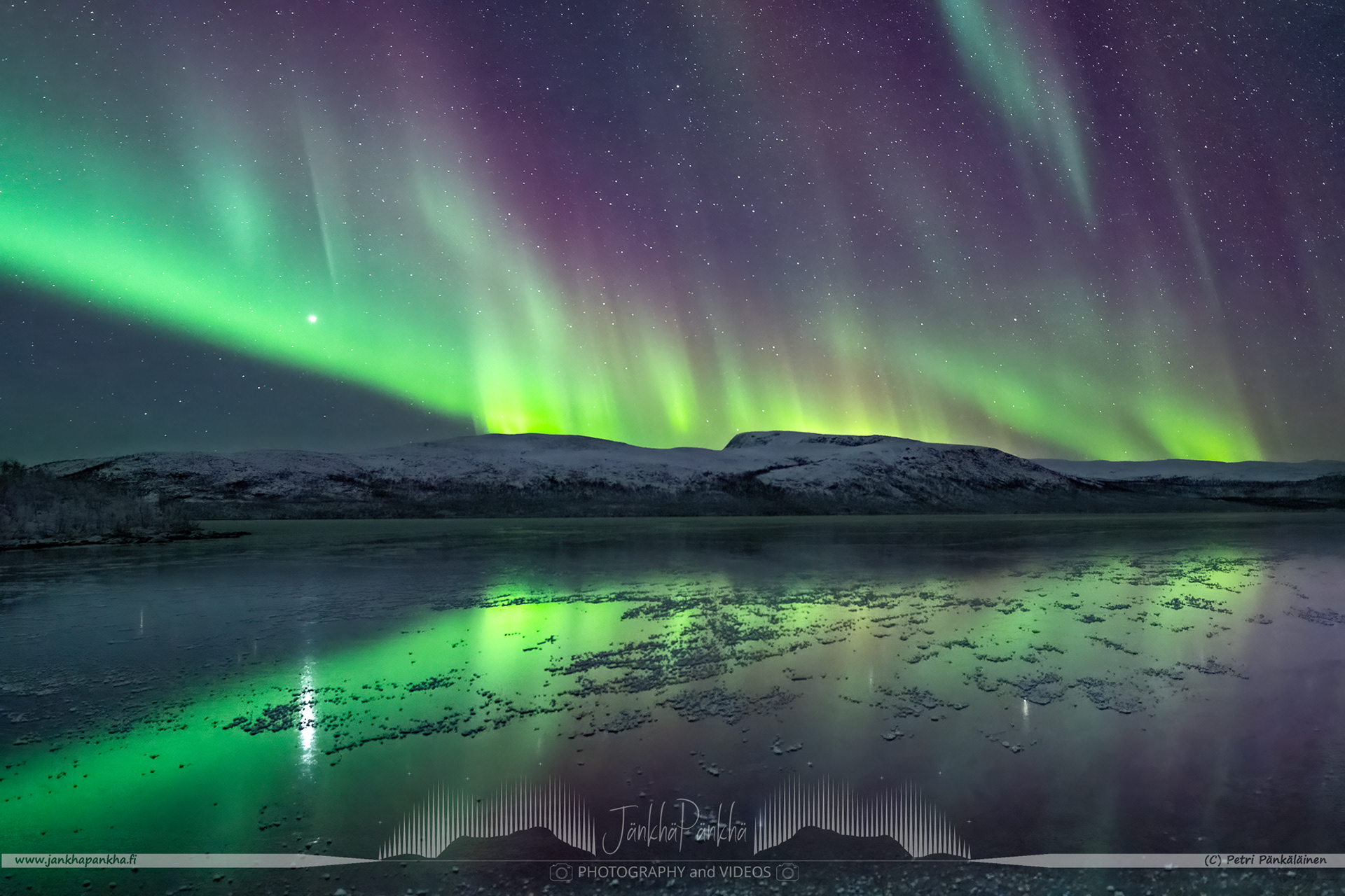 Intense and colorful northern lights over the mirror-like iced lake Ala-Kilpisjärvi in Enontekiö, Finland