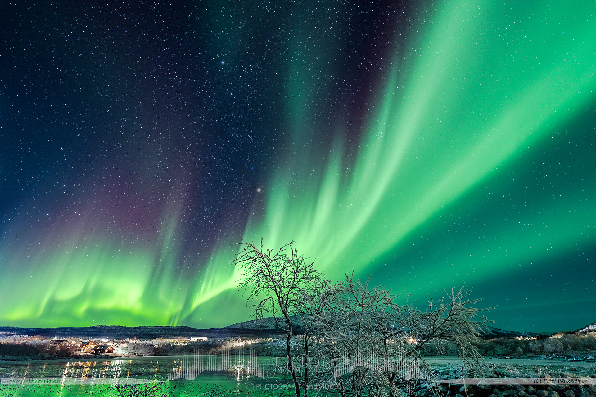 Saanatunturi, fell Saana, in Kilpisjärvi surrounded by the fast moving northern lights and mirror-like ice cover on the lake Kilpisjärvi. The lights of the village Kilpisjärvi at the front complements the photo well.
