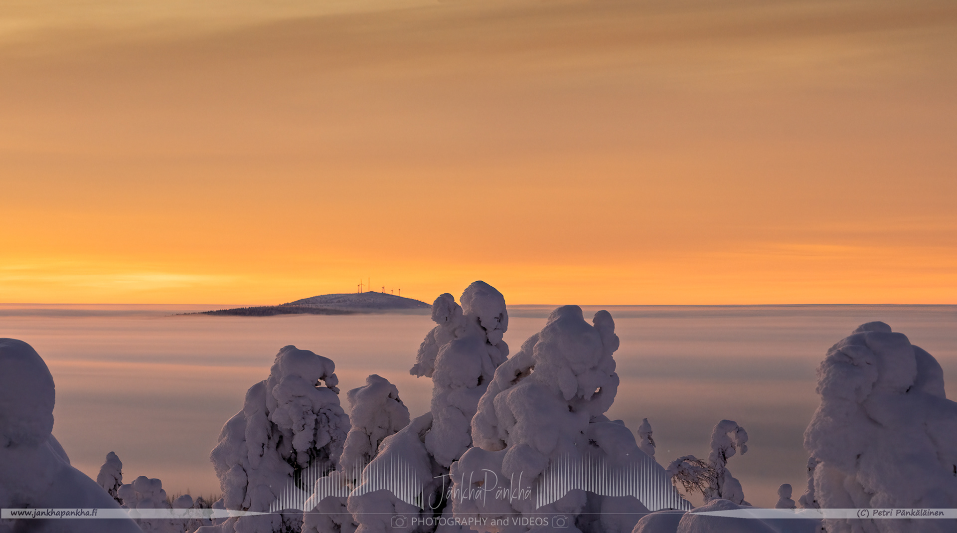 Orange and yellow sunset casting a warm glow over the snowy landscapes of Pallas-Yllästunturi National Park. The Olostunturi fell in the horizon and the village of Muonio covered with the clouds.
