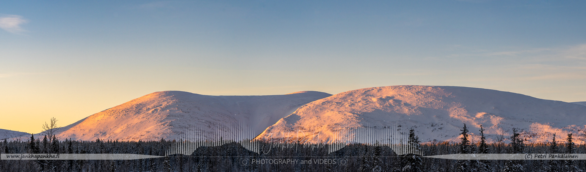 Pallas-Yllästunturi National Park's snowy landscapes bathed in the warm colors of a winter sunrise.