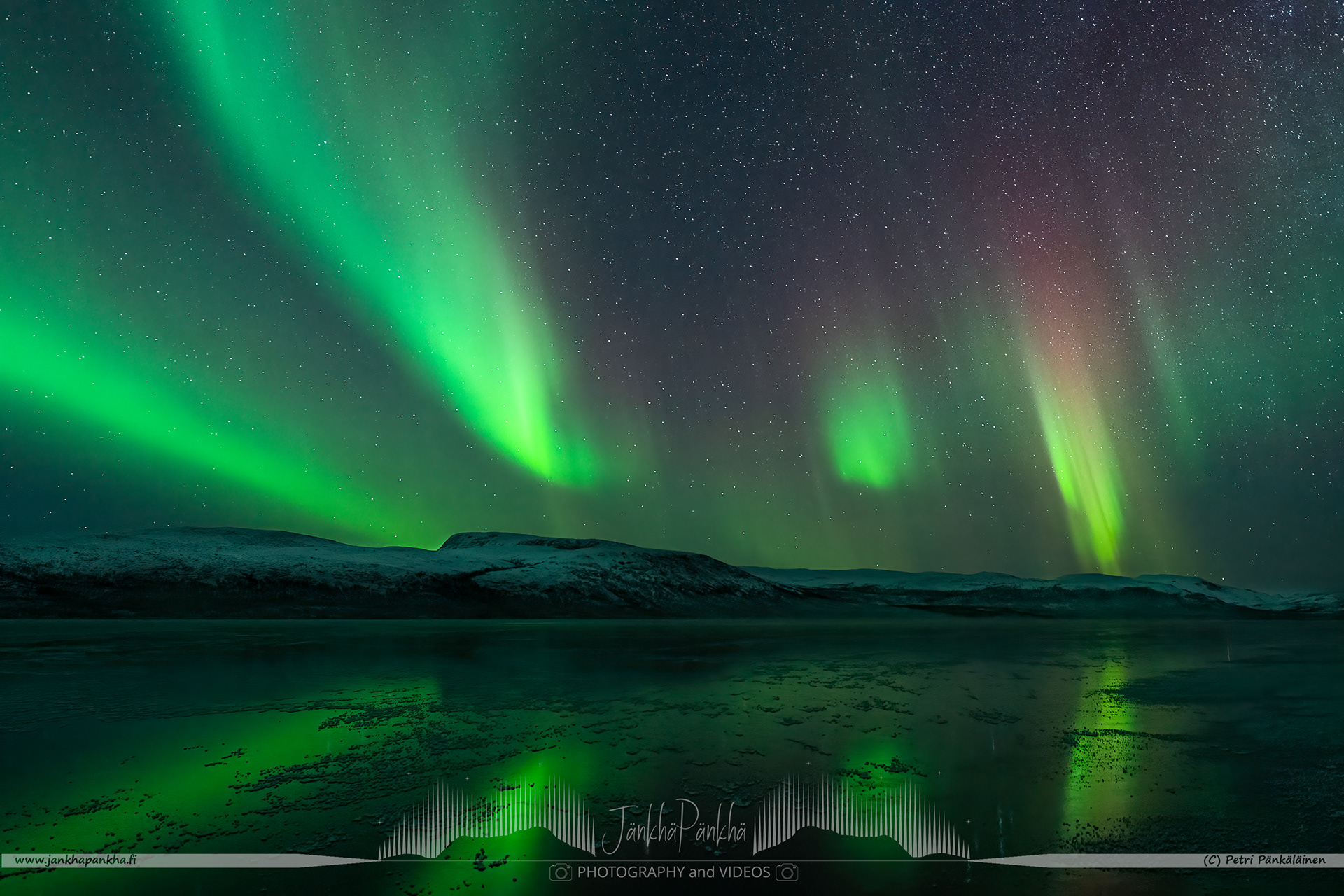 Intense and colorful northern lights over the mirror-like iced lake Ala-Kilpisjärvi in Finland