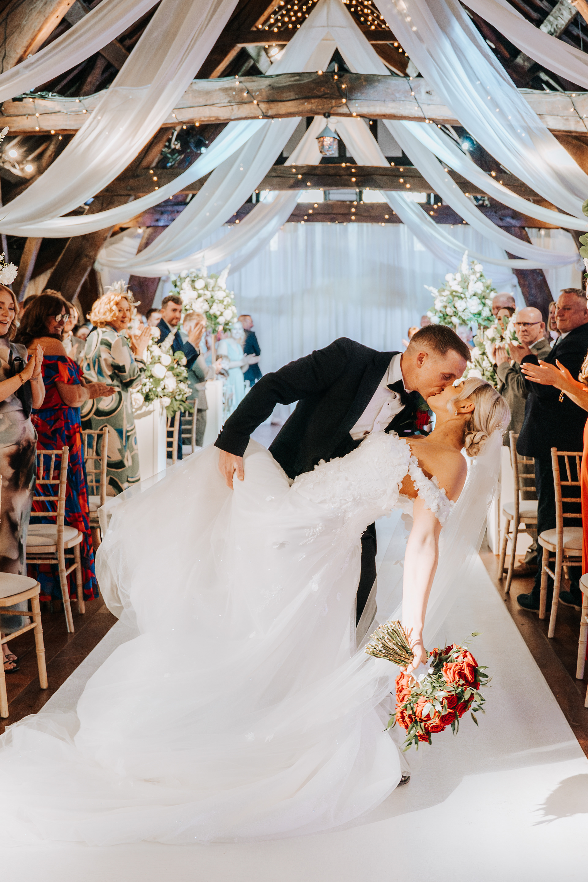 Emotional aisle exit complete with a dip kiss and cheering guests - luxury wedding photography and videography team