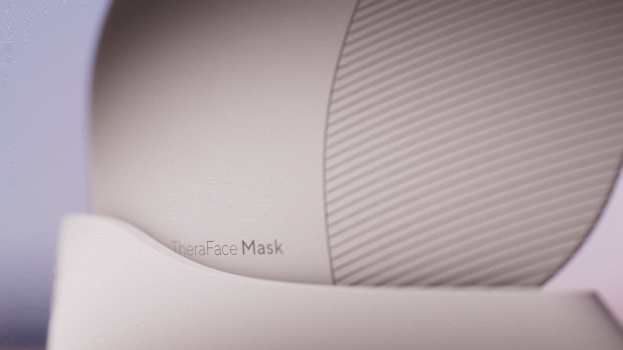 Animated sequence: A close-up of a white TheraFace Mask, focusing on its sleek design and the brand name "TheraFace Mask" printed on it.