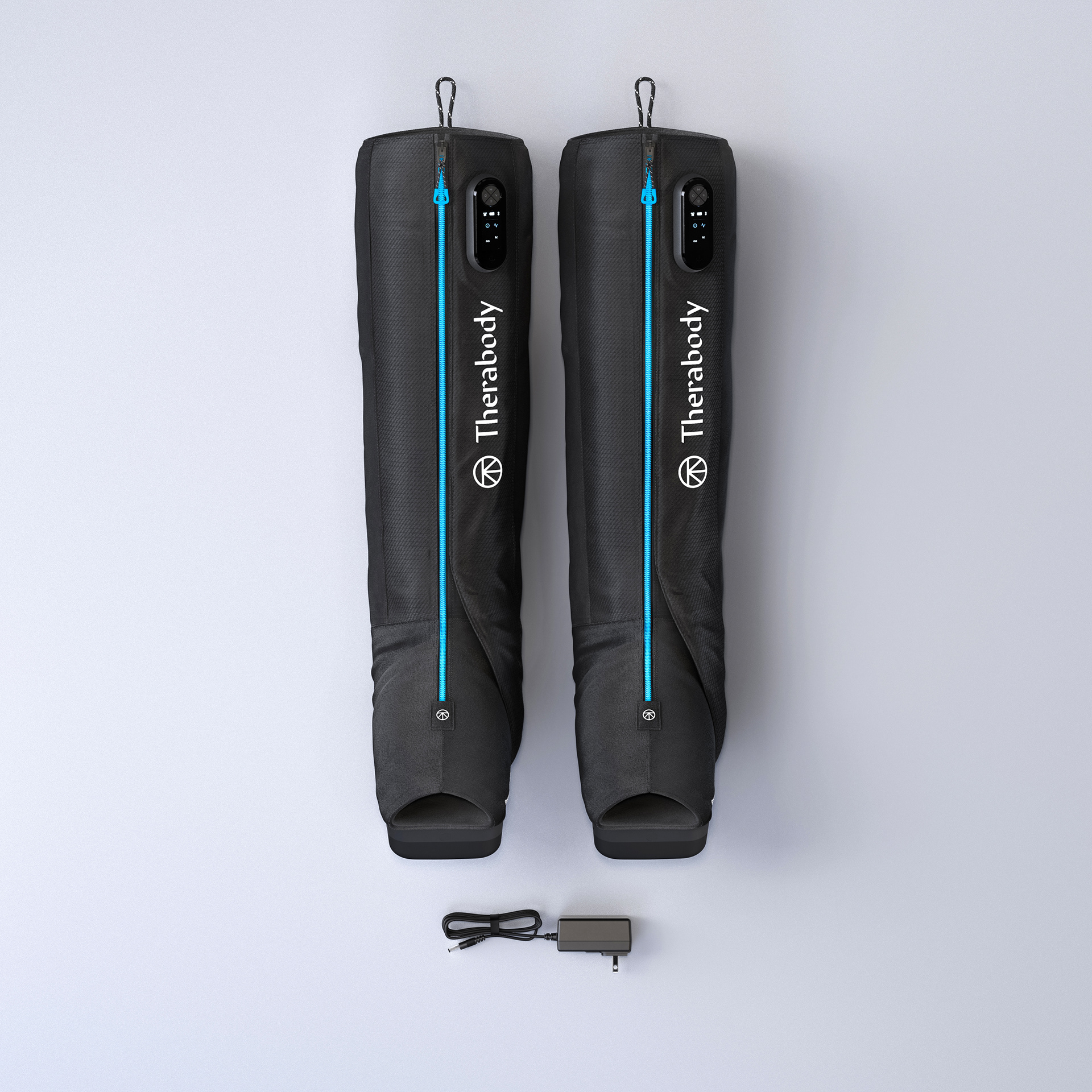 Two black Therabody RecoveryAir Jetboots laid flat on a white surface, with a blue line indicating the length of each boot. A USB cable is placed between them.