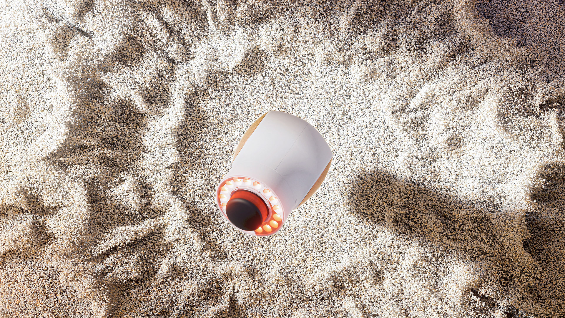 A futuristic, sleek device with a glowing red light on its top, resting on a textured surface.
