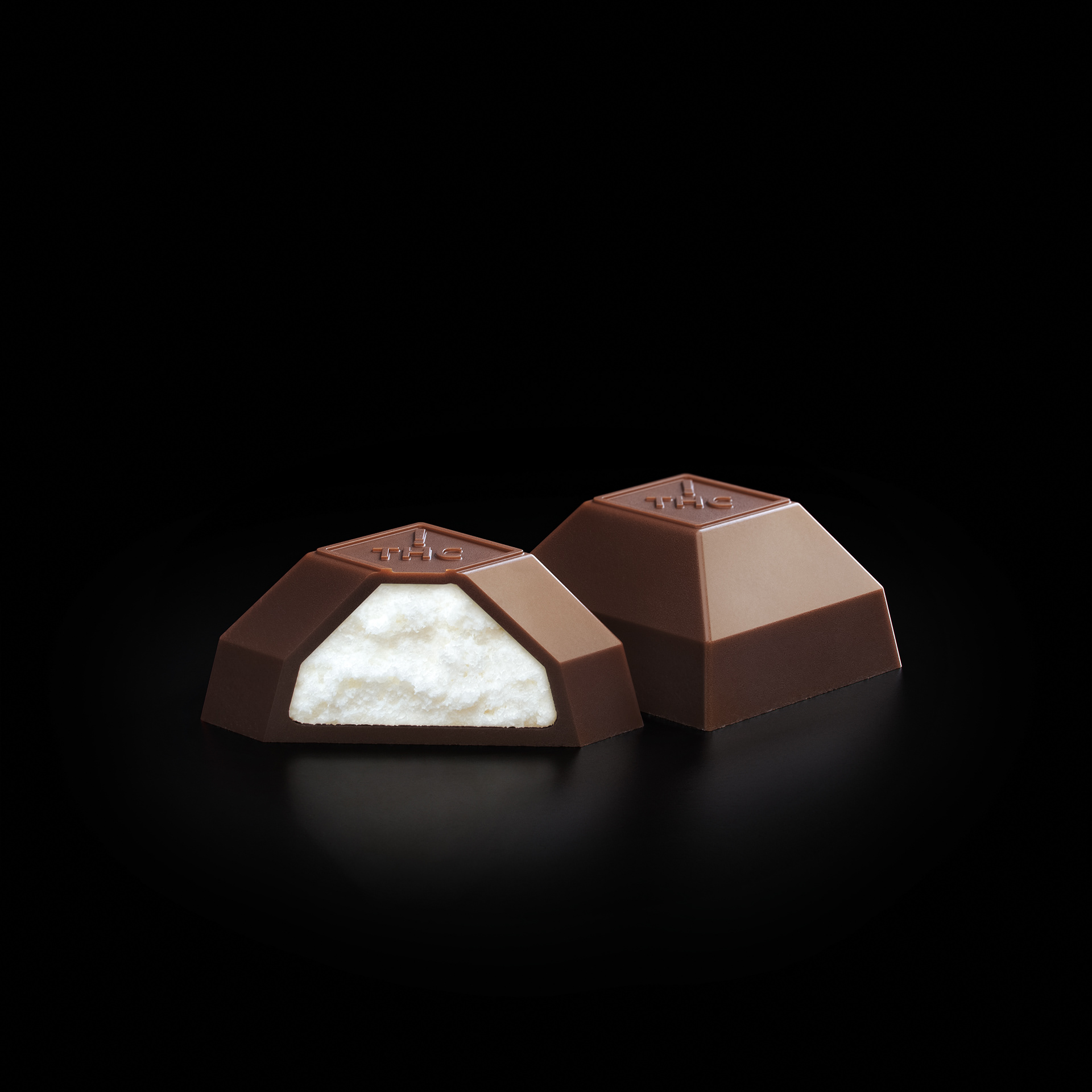A triangular chocolate bar cut in half, revealing a creamy white center, set against a dark background.