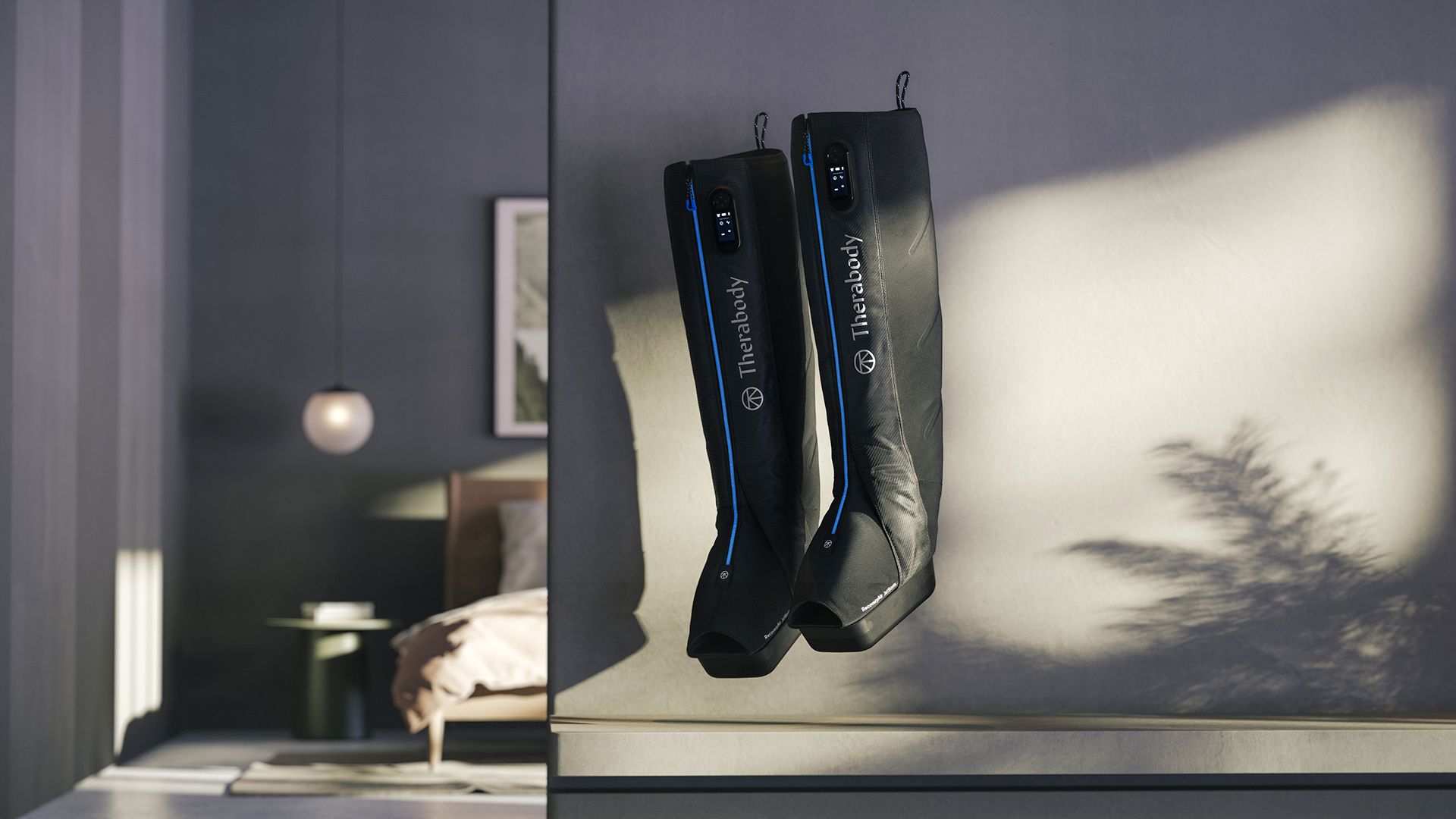 A pair of black Therabody Jetboots hanging on a hook, displaying the brand name and model number "E3" on the side.