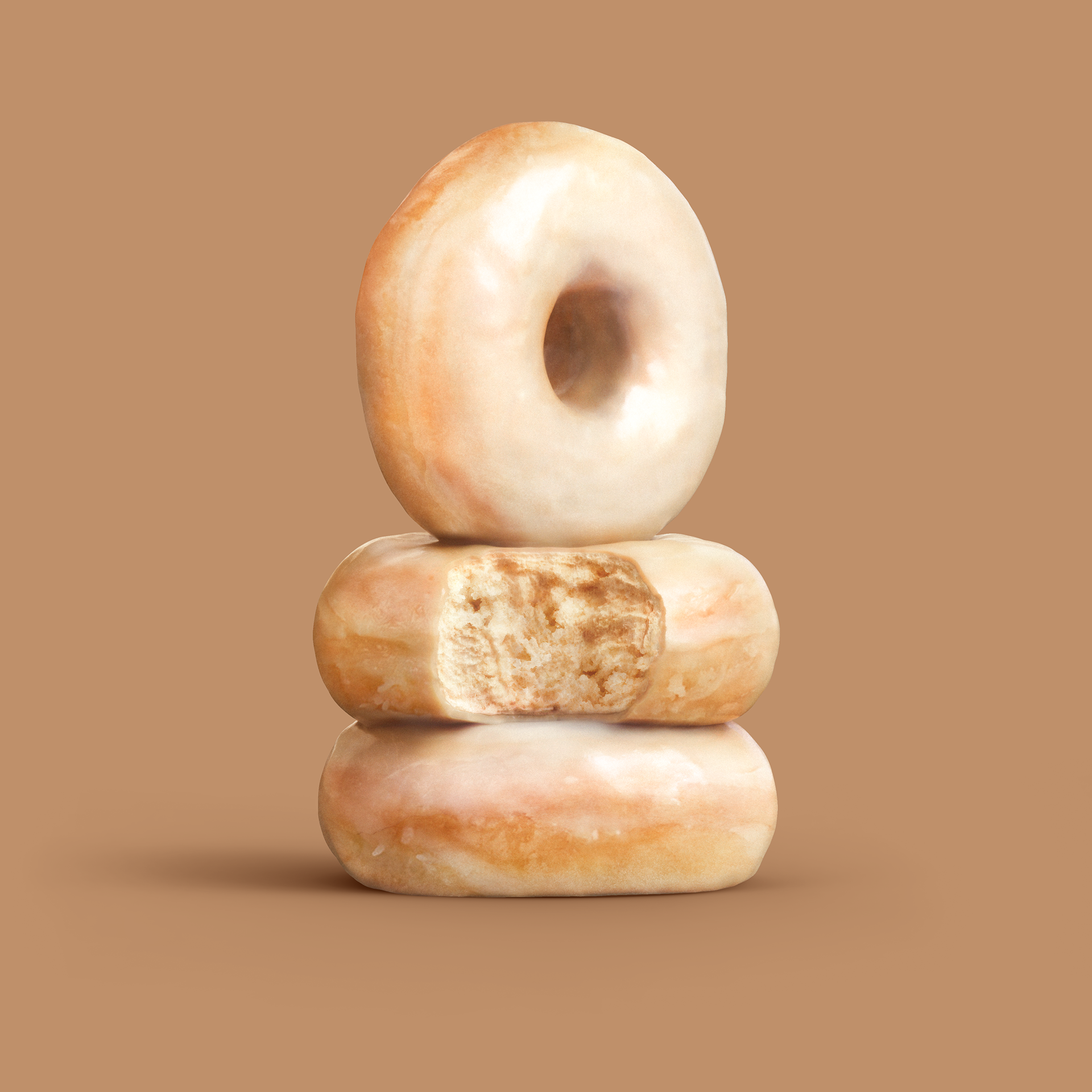 Three glazed donuts stacked on a plain background, showing their texture and color.