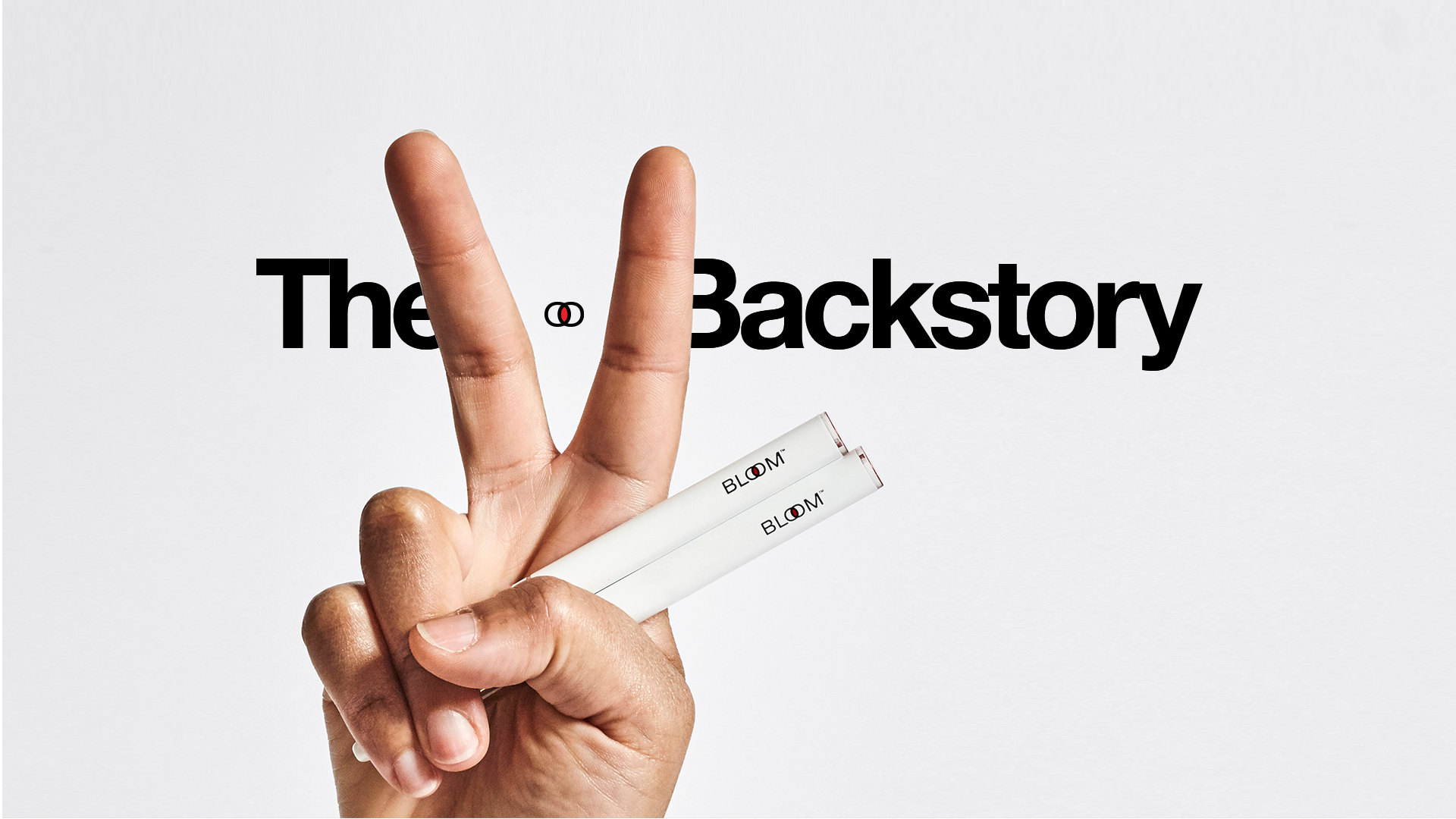 A hand making a peace sign holds two white tubes labeled "BLOOM" against a white background.