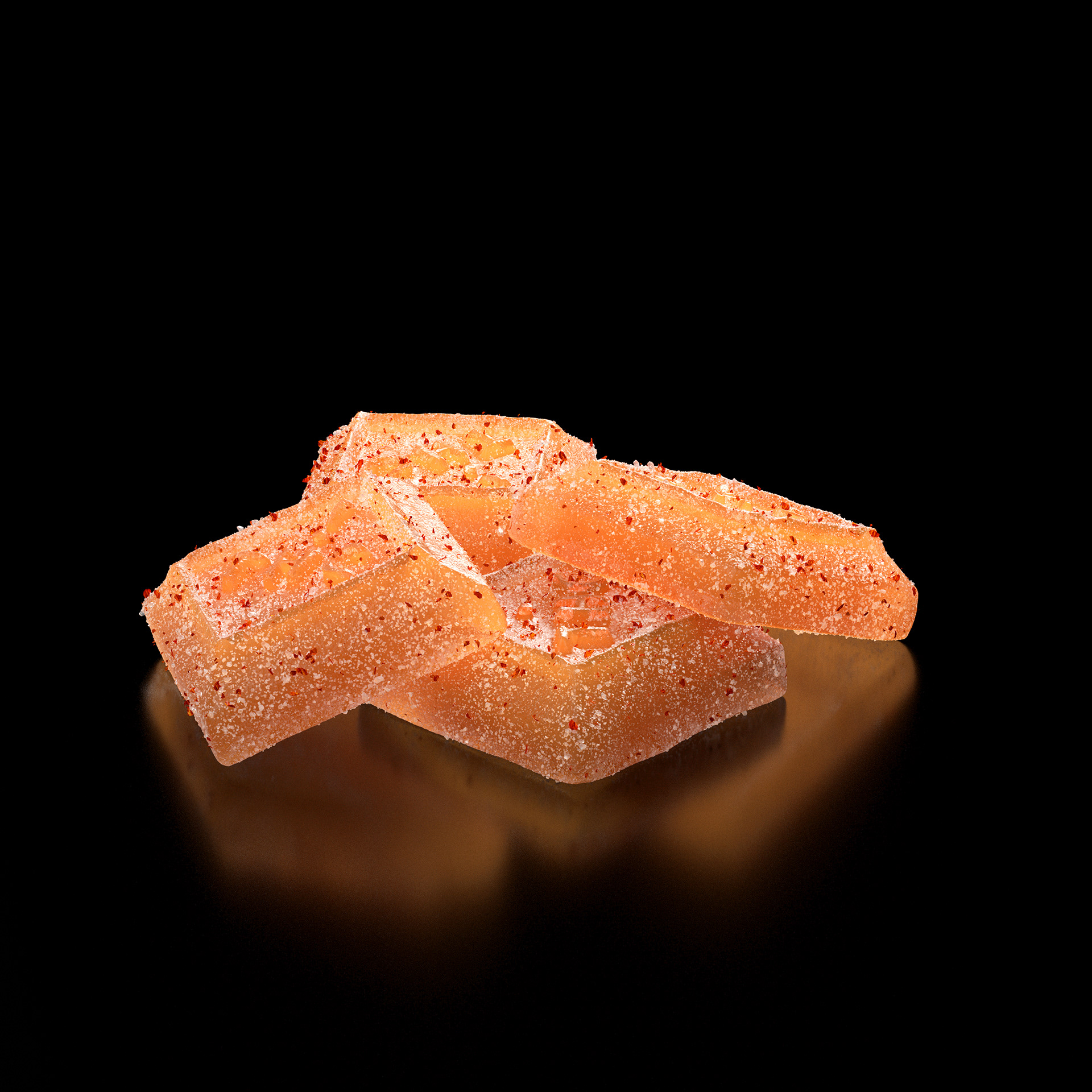 A stack of orange candy bars with a smooth texture and small red specks, set against a black background.