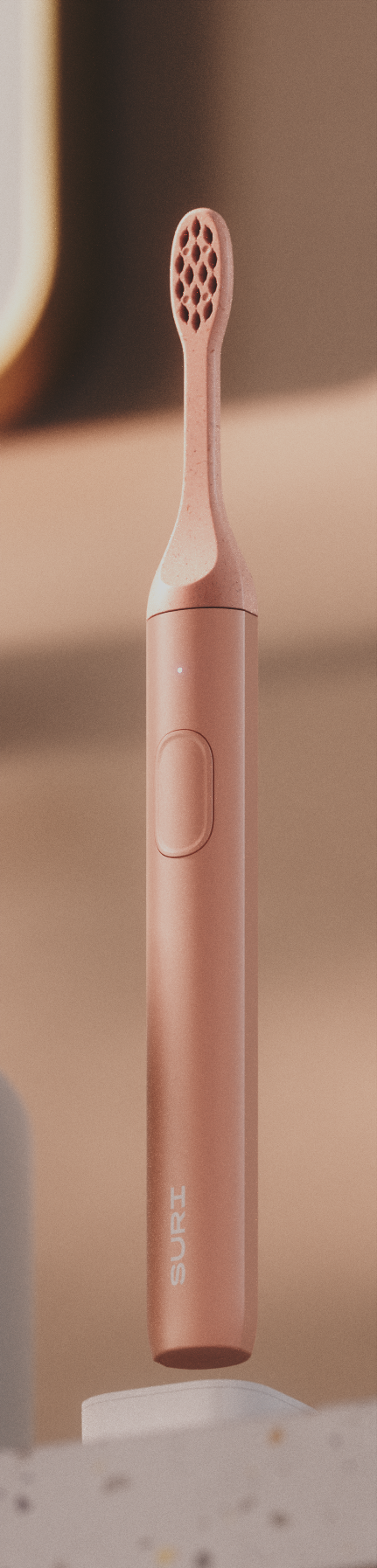 A sleek, rose gold SURI 2.0 electric toothbrush with a textured head and a power button, displayed against a warm, gradient background.