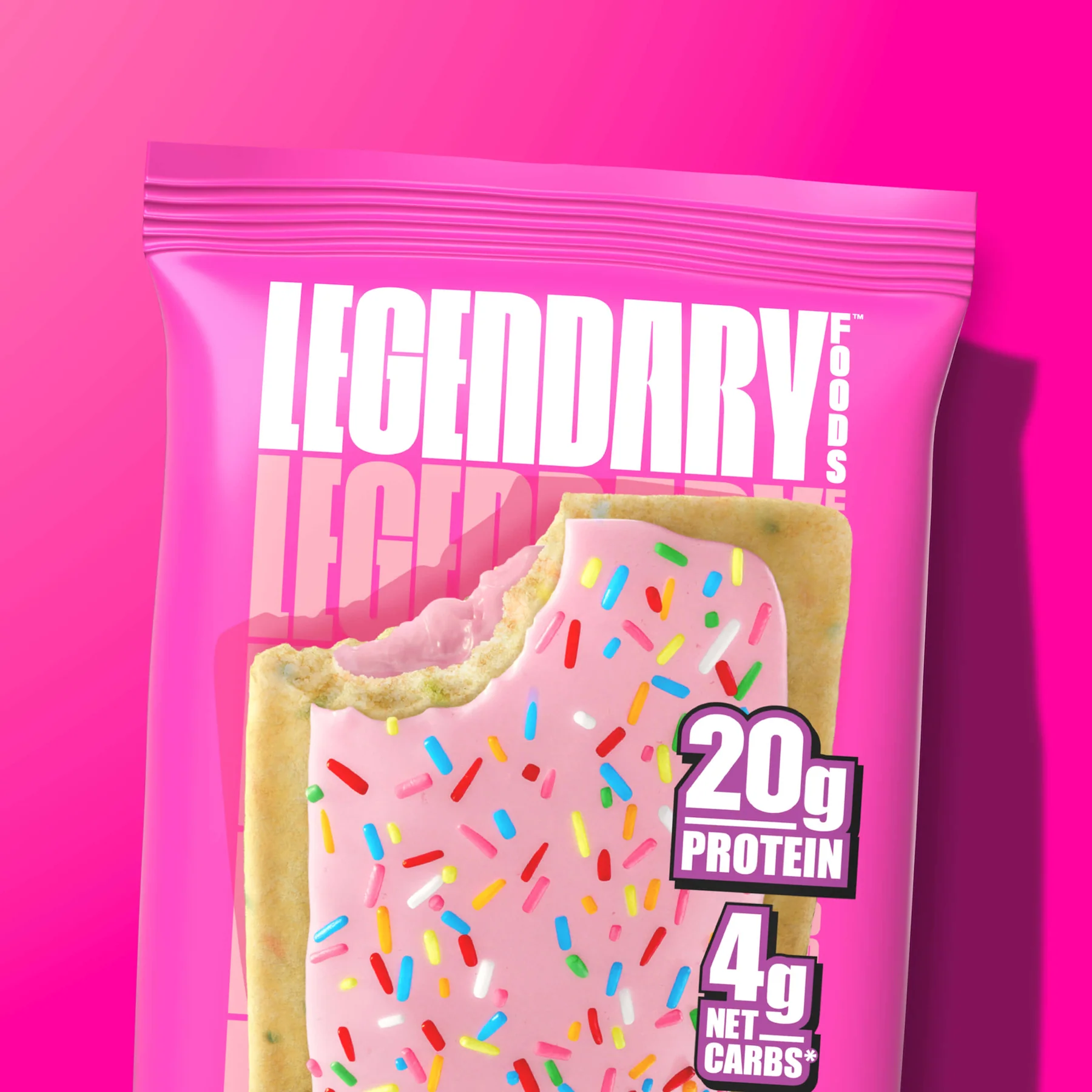 A pink bag of "Legendary Foods" protein bars with a bite taken out, revealing sprinkles and a pink filling, against a vibrant pink background.