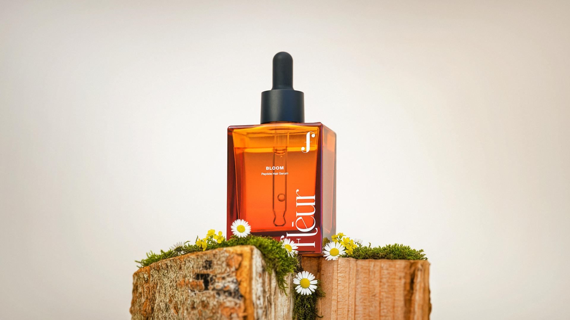 A sleek, amber-colored bottle of "BLOOM" peptides sits atop a rustic wooden block, surrounded by small white flowers and green moss, against a soft, neutral background.