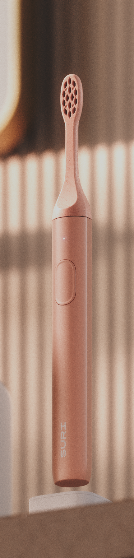 A sleek, peach-colored electric toothbrush with a textured head and a power button, standing upright against a striped background.
