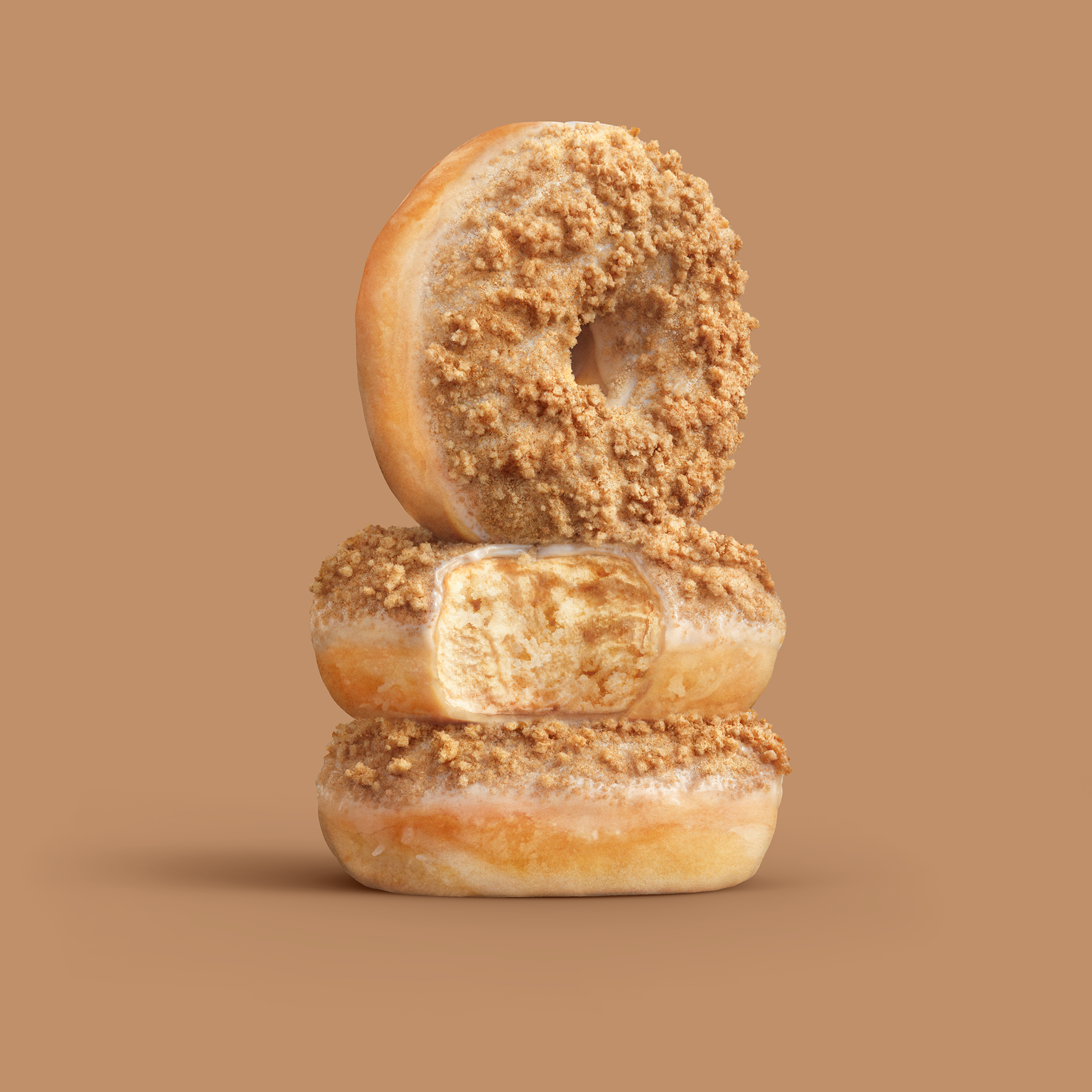 Three glazed doughnuts stacked on top of each other, with a light brown background.