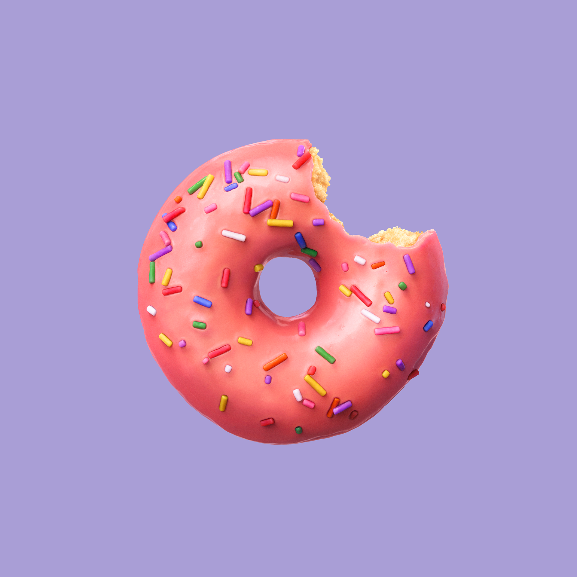 A pink frosted donut with colorful sprinkles, bitten into, on a purple background.