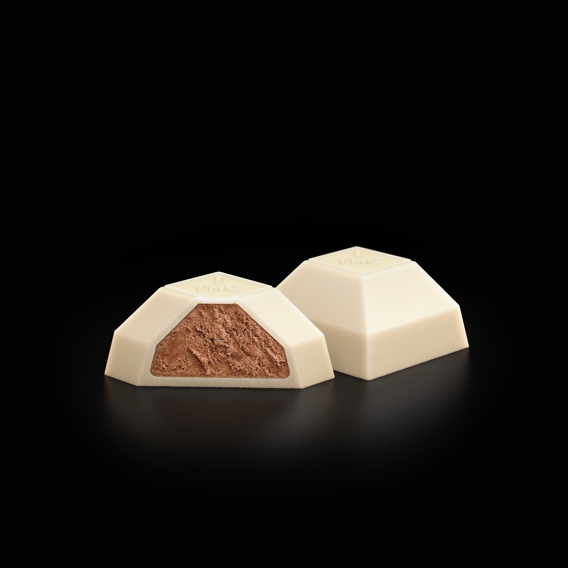 Two triangular chocolate bars, one cut open to reveal a rich brown cocoa center, set against a black background.