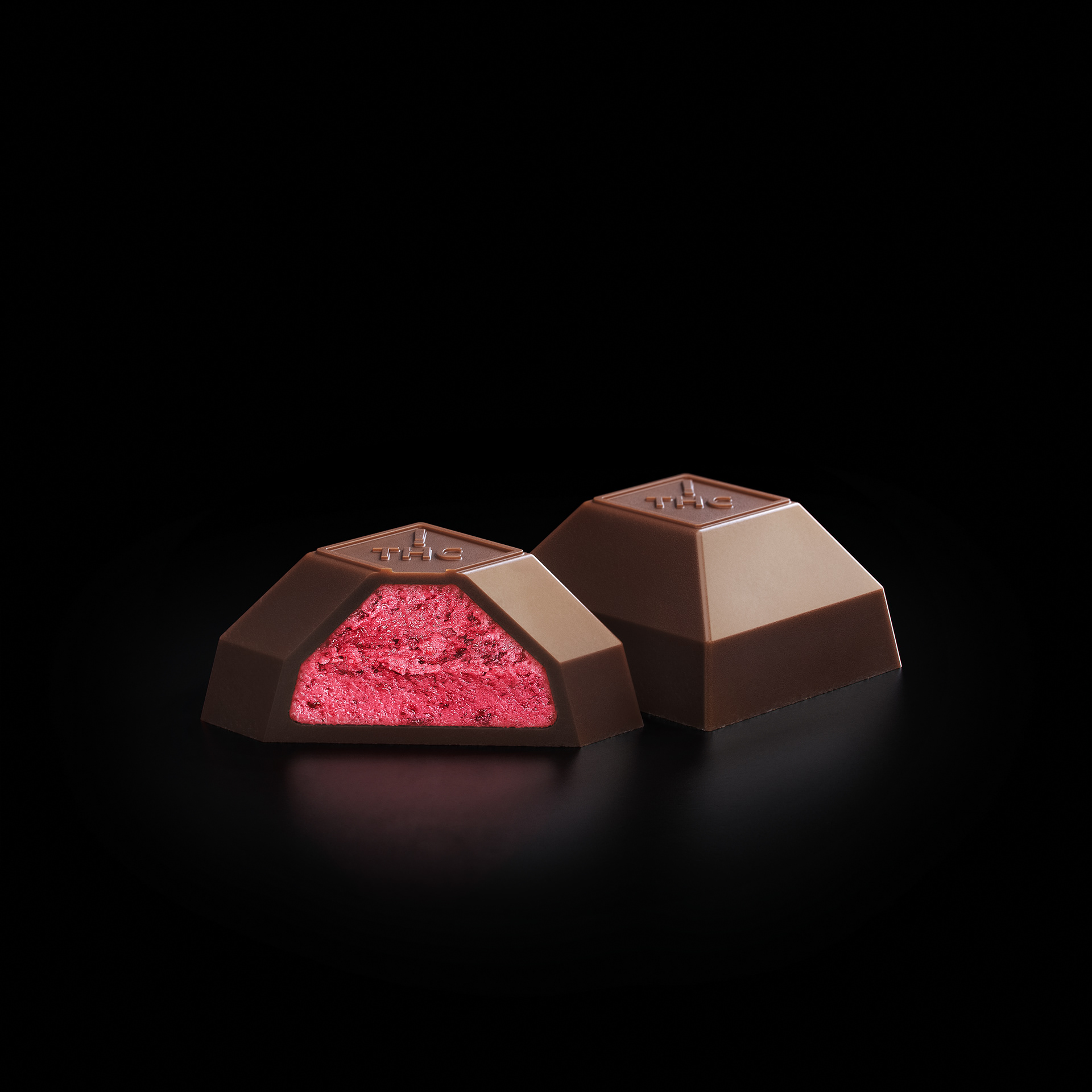 A chocolate bar cut in half, revealing a pink filling inside, set against a black background.